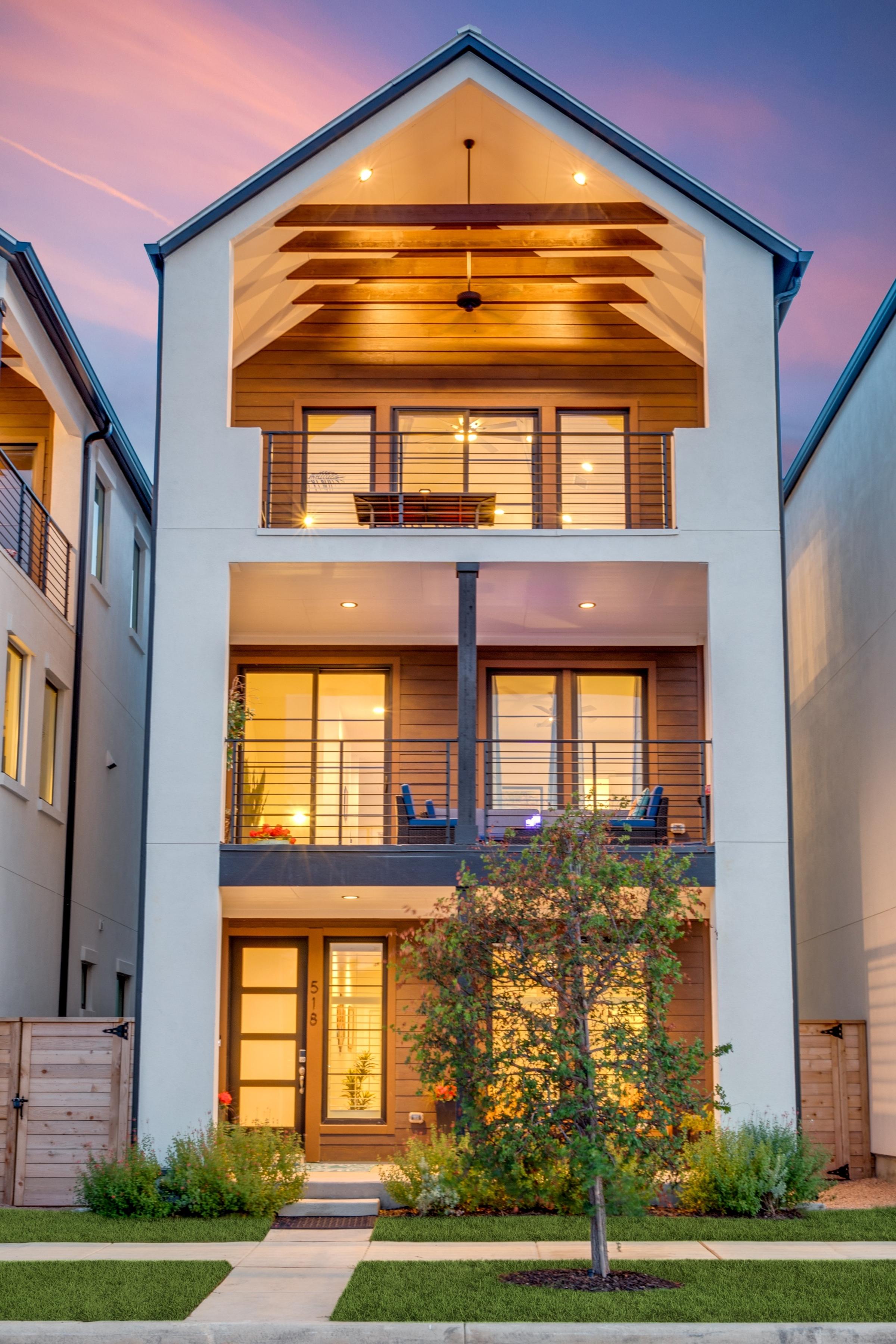 Modern three-story townhome with cedar balconies, warm interior glow, and purple twilight sky in San Antonio, Texas