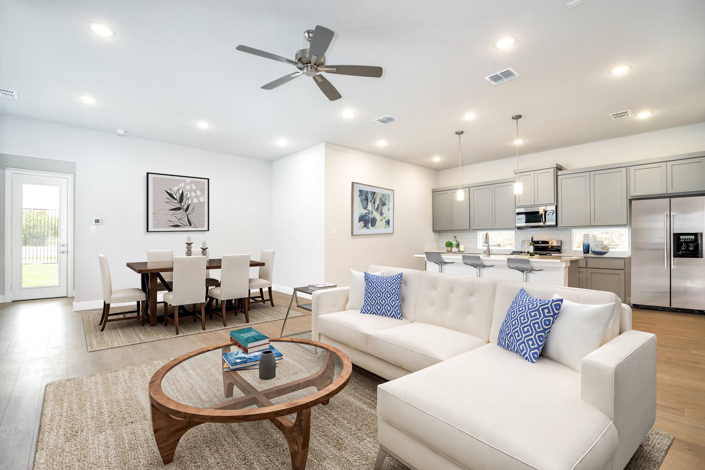Virtually staged open-concept kitchen and living room with white sectional, dining set, and blue accent pillows in Heath, Texas