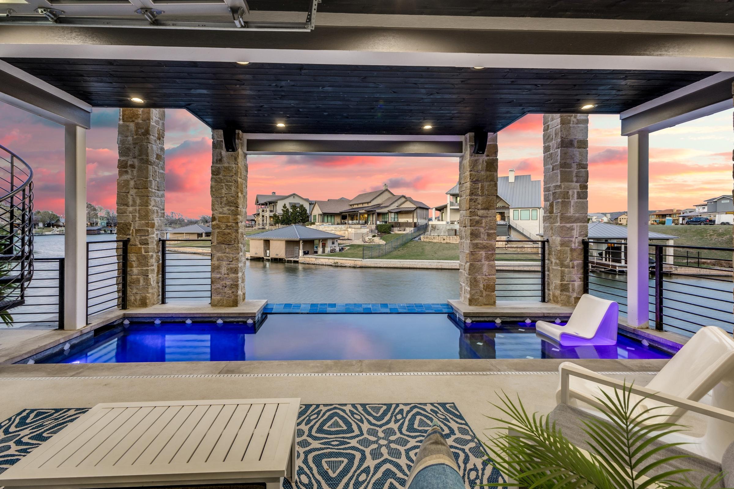 Covered cabana with infinity-edge pool and LED lighting overlooking a waterfront canal community at twilight in Kingsland, Texas
