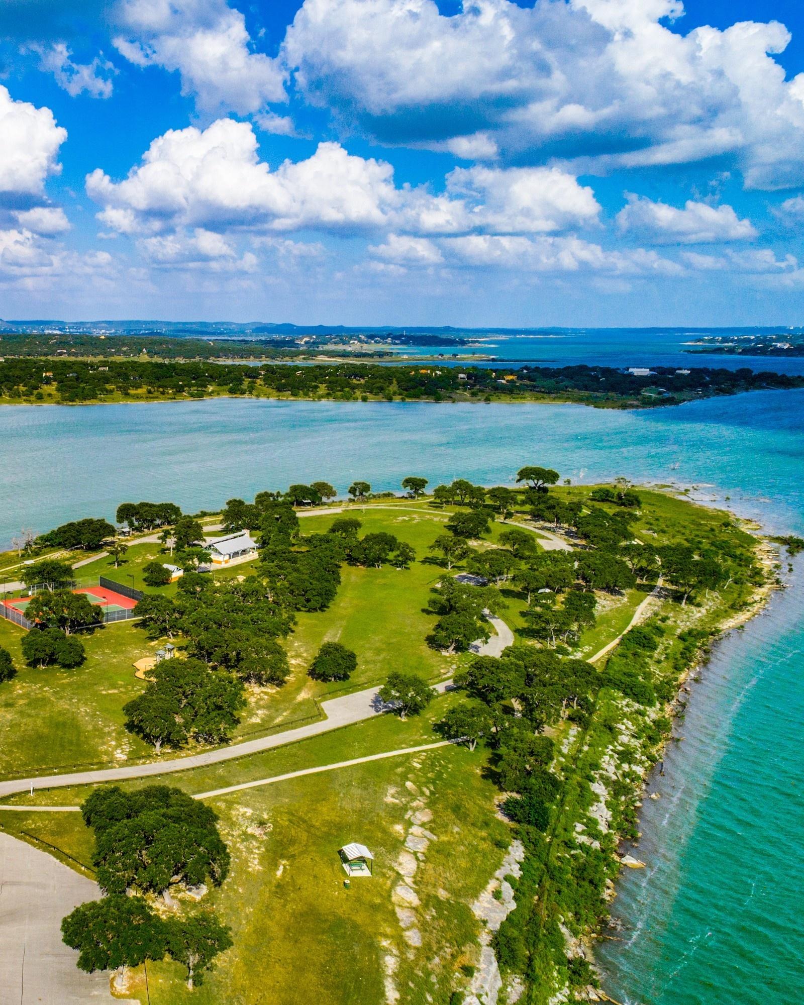 Aerial view of a lakefront peninsula with turquoise water, tennis court, and green landscape near Spring Branch, Texas