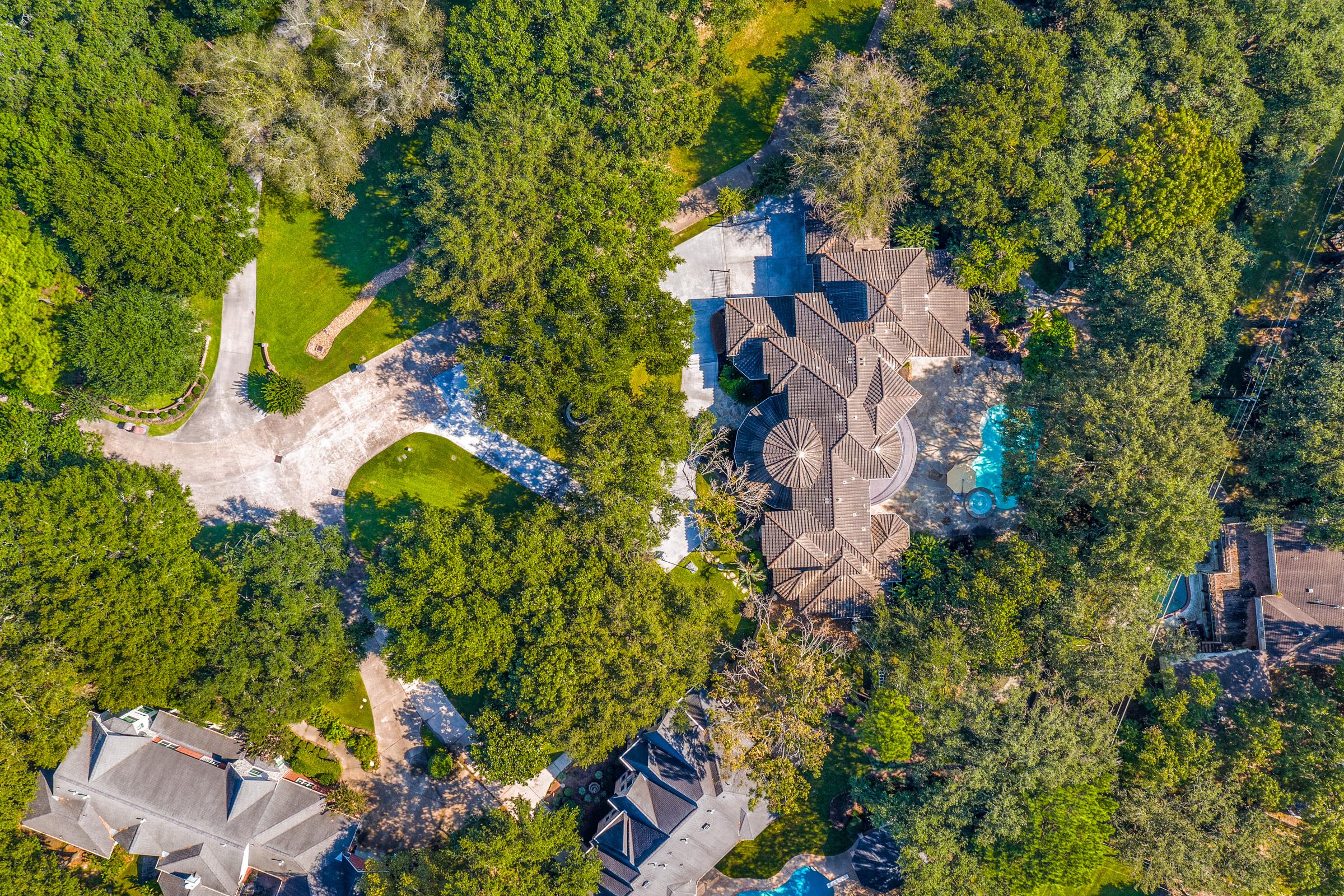 Overhead aerial view of a large tile-roof estate with a pool set among mature trees in Spring, Texas