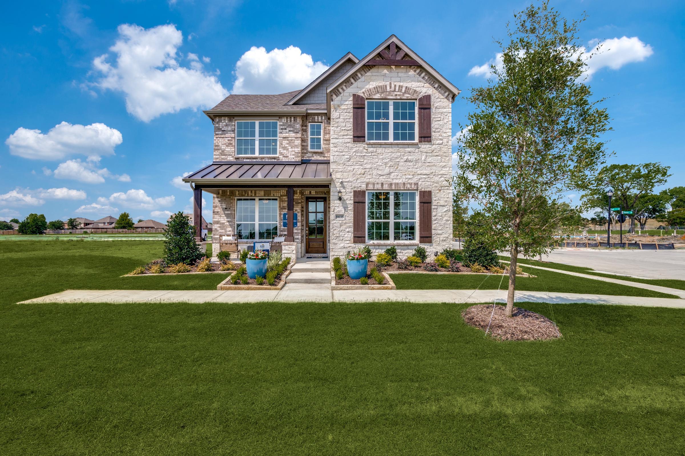 Two-story stone and siding model home with landscaped front yard and blue planters in a new construction community in Rowlett, Texas