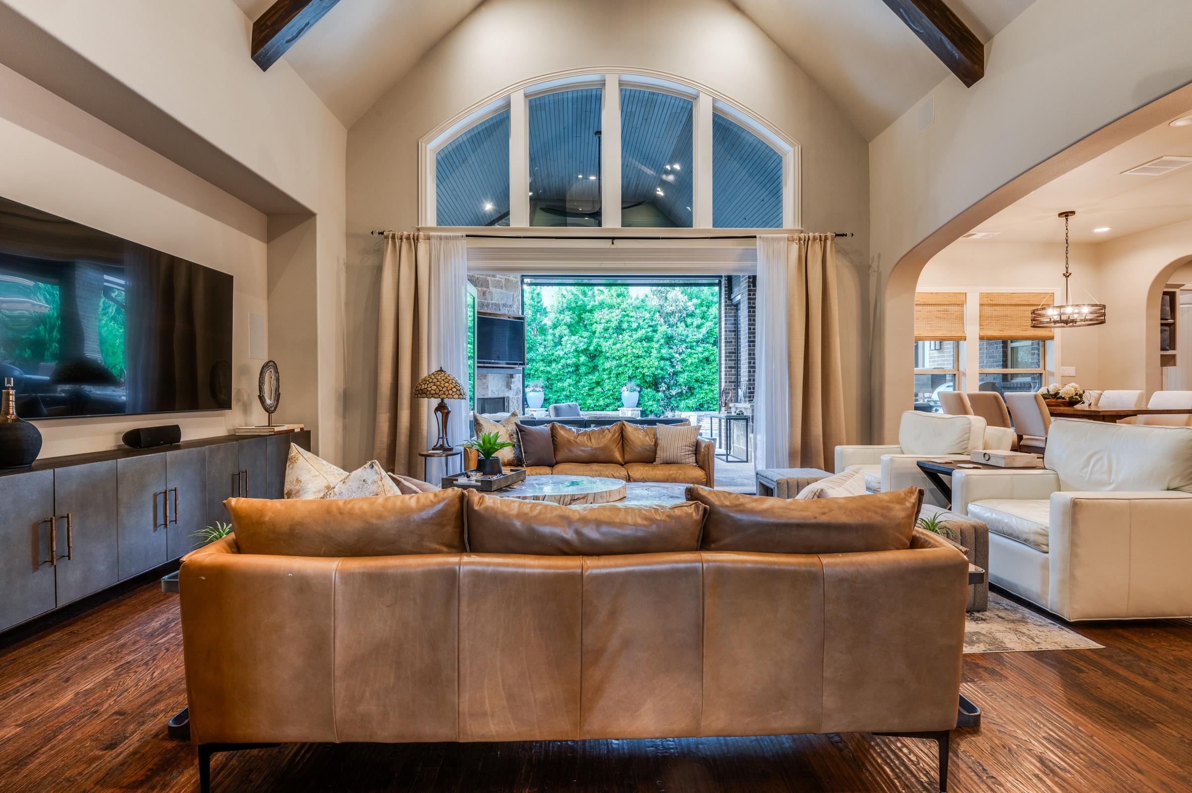 Open living room with vaulted ceiling, wood beams, leather sofa, and arched window in Southlake, Texas