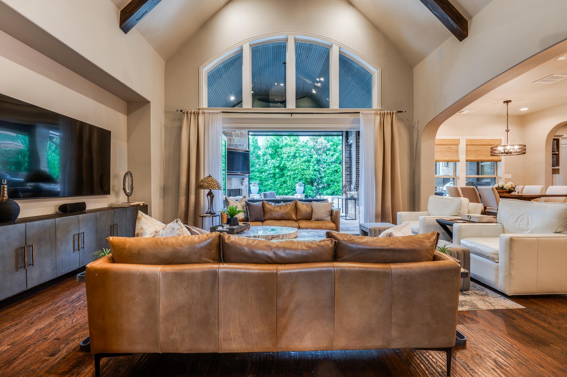 Open living room with vaulted ceiling, wood beams, leather sofa, and arched window in Southlake, Texas