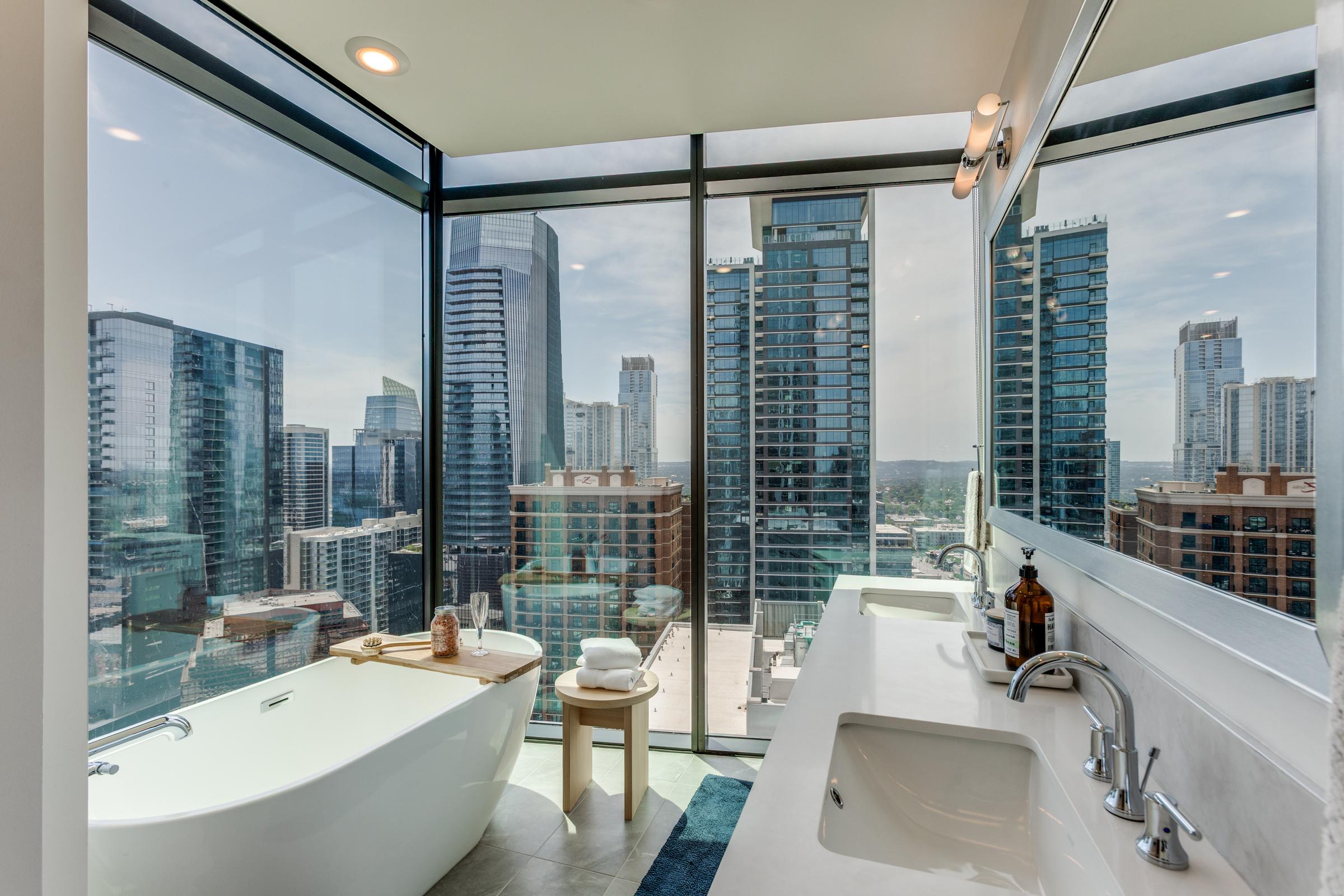 Primary bathroom with a freestanding tub and floor-to-ceiling windows overlooking the downtown Austin skyline