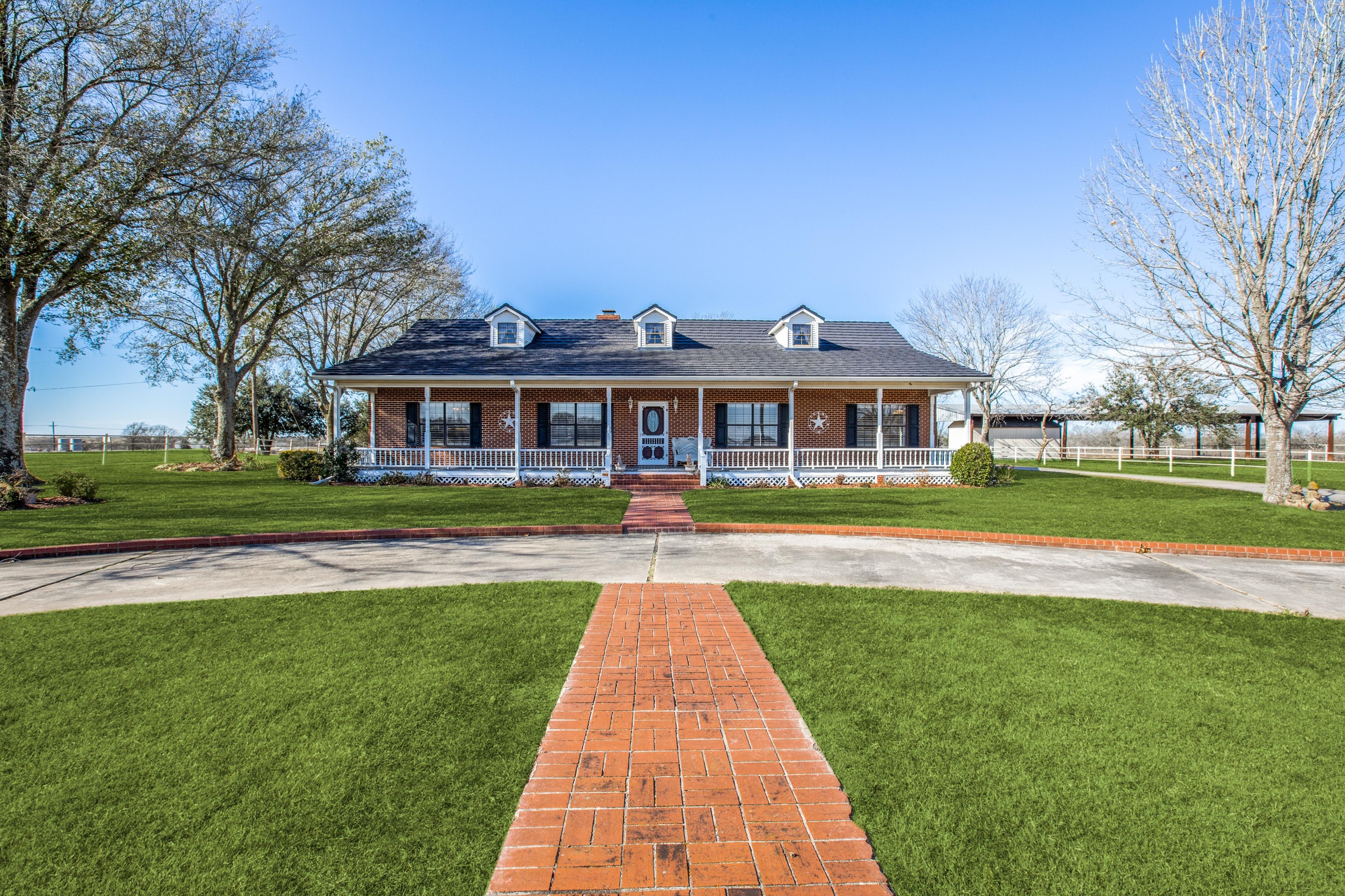 Daytime photo of a ranch home with wraparound porch and blue sky before digital twilight enhancement in Mexia, Texas