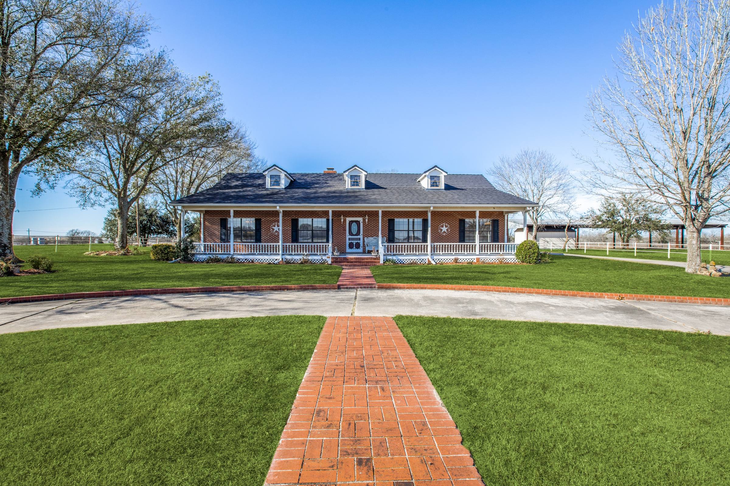 Daytime photo of a ranch home with wraparound porch and blue sky before digital twilight enhancement in Mexia, Texas