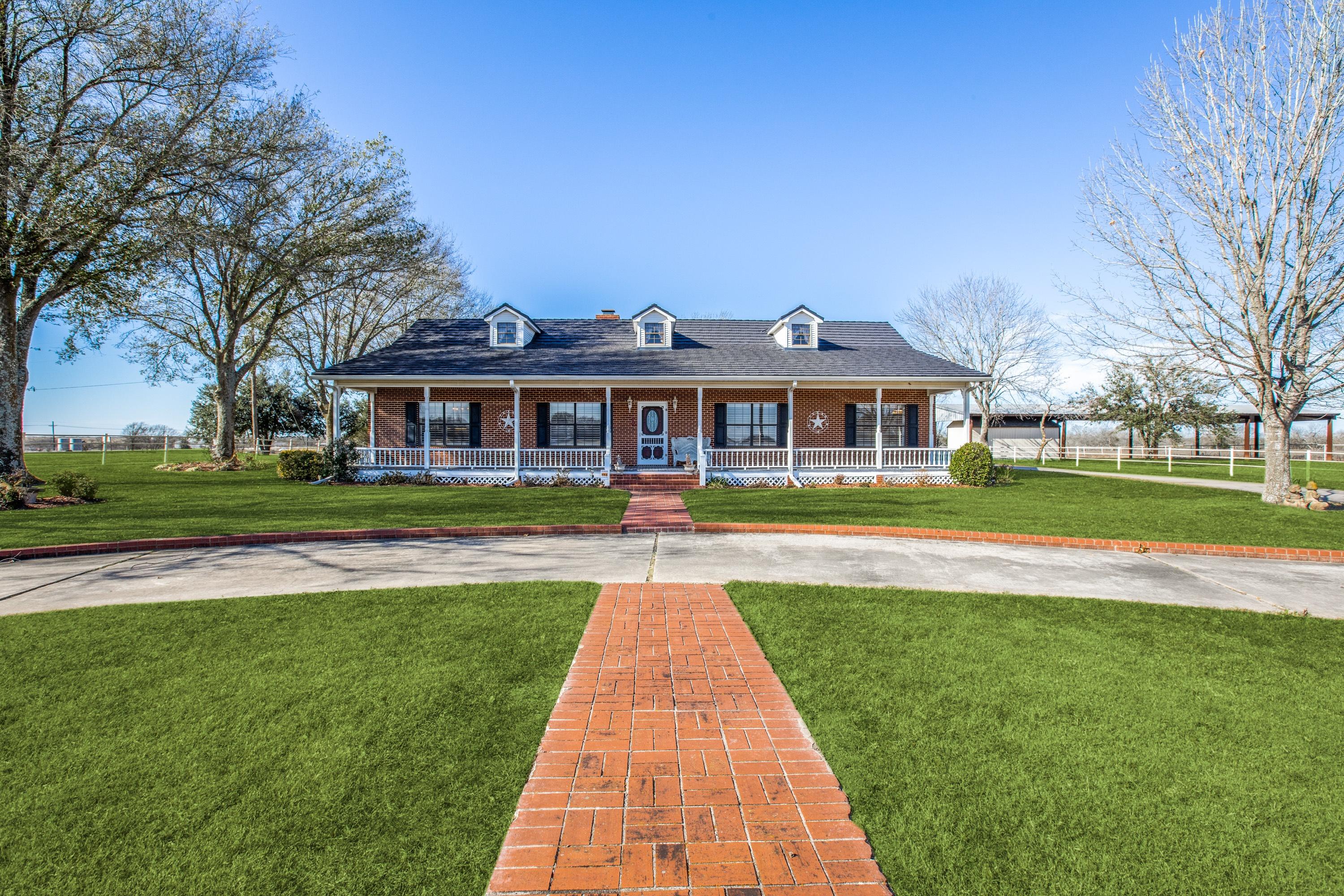 Daytime photo of a ranch home with wraparound porch and blue sky before digital twilight enhancement in Mexia, Texas