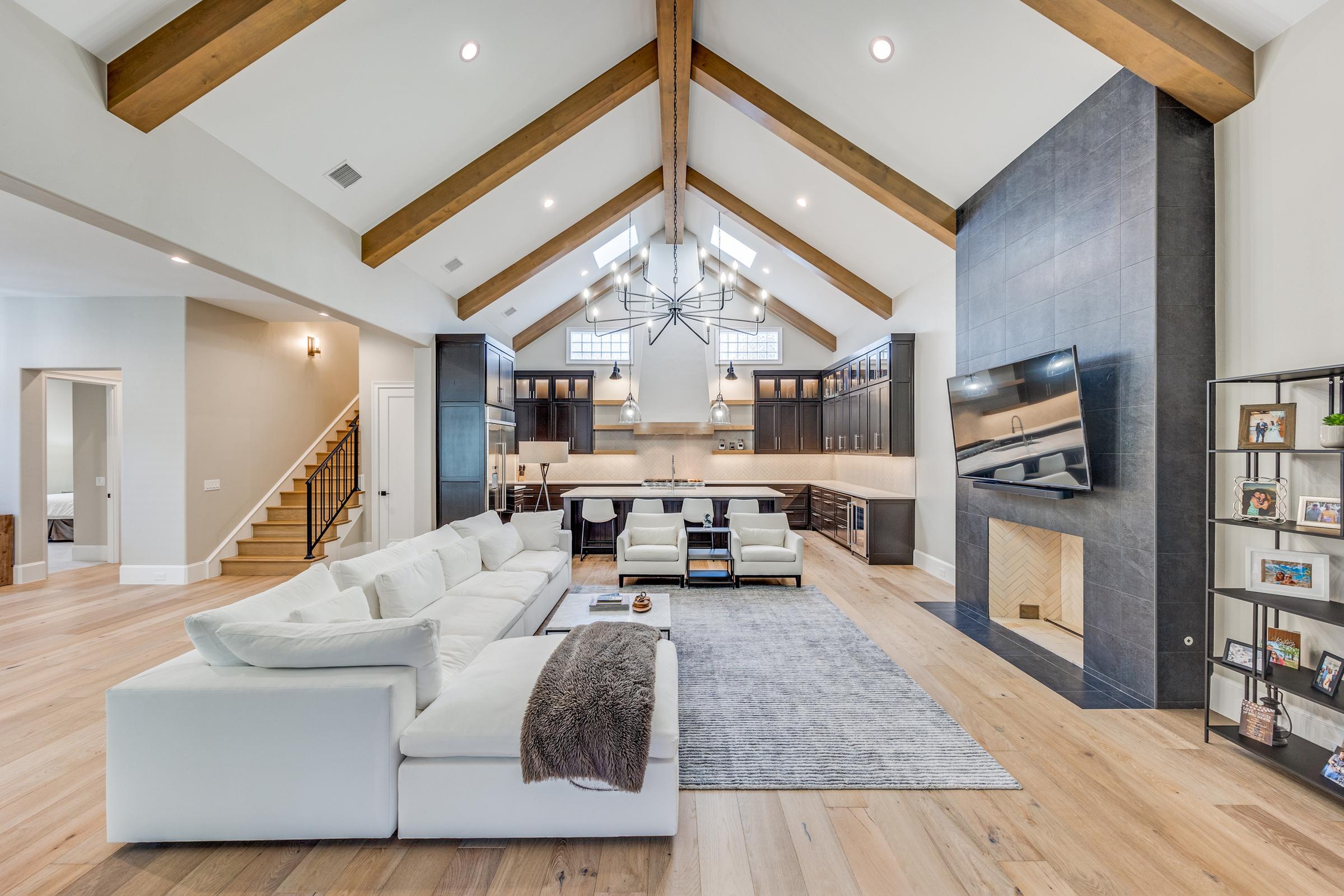 Open-concept living room with vaulted wood-beam ceiling, white sectional, and kitchen beyond in a Plano home