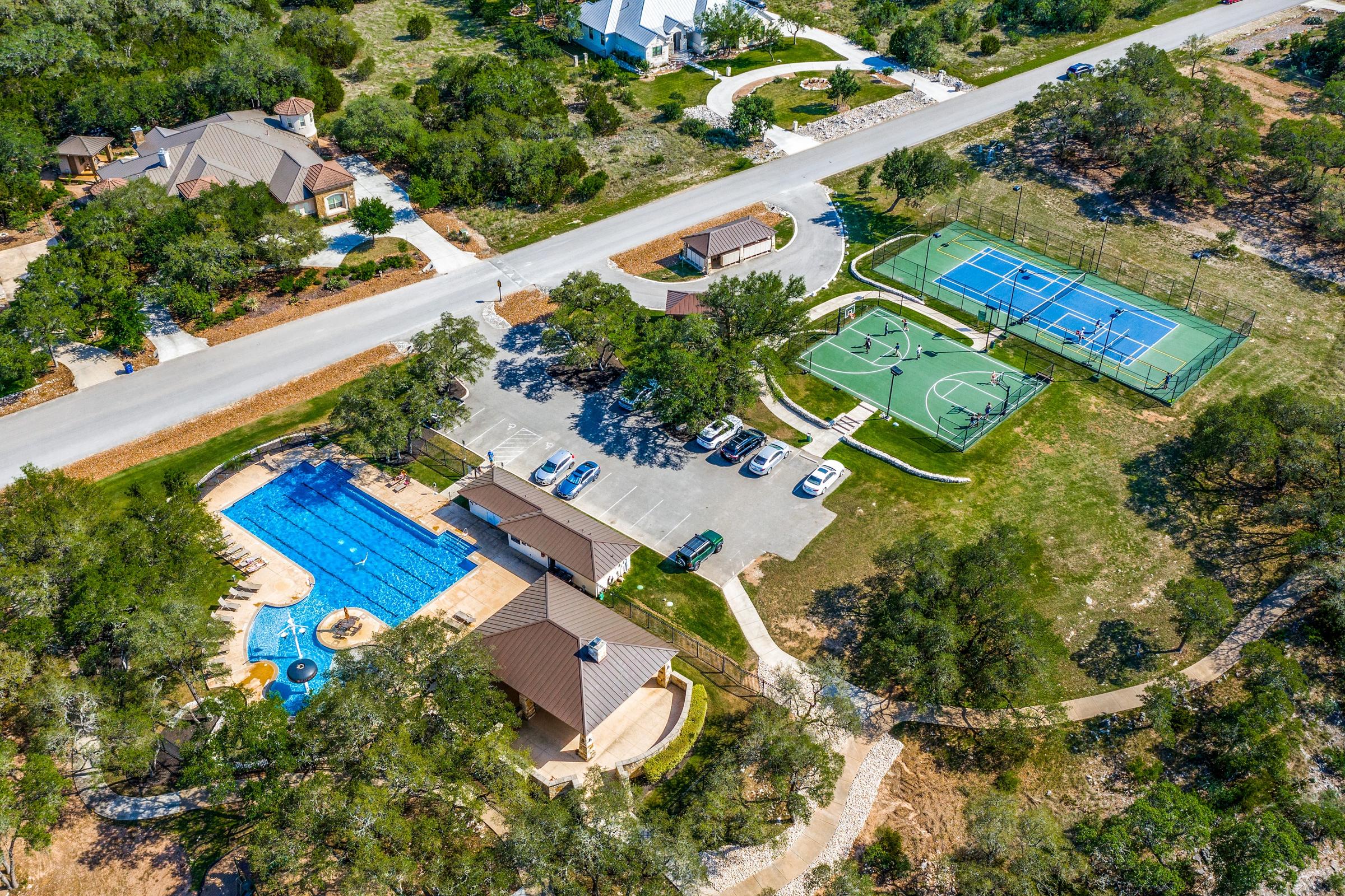 Aerial drone view of a community amenity center with pool, covered pavilion, and new construction homes in the background in New Braunfels, Texas