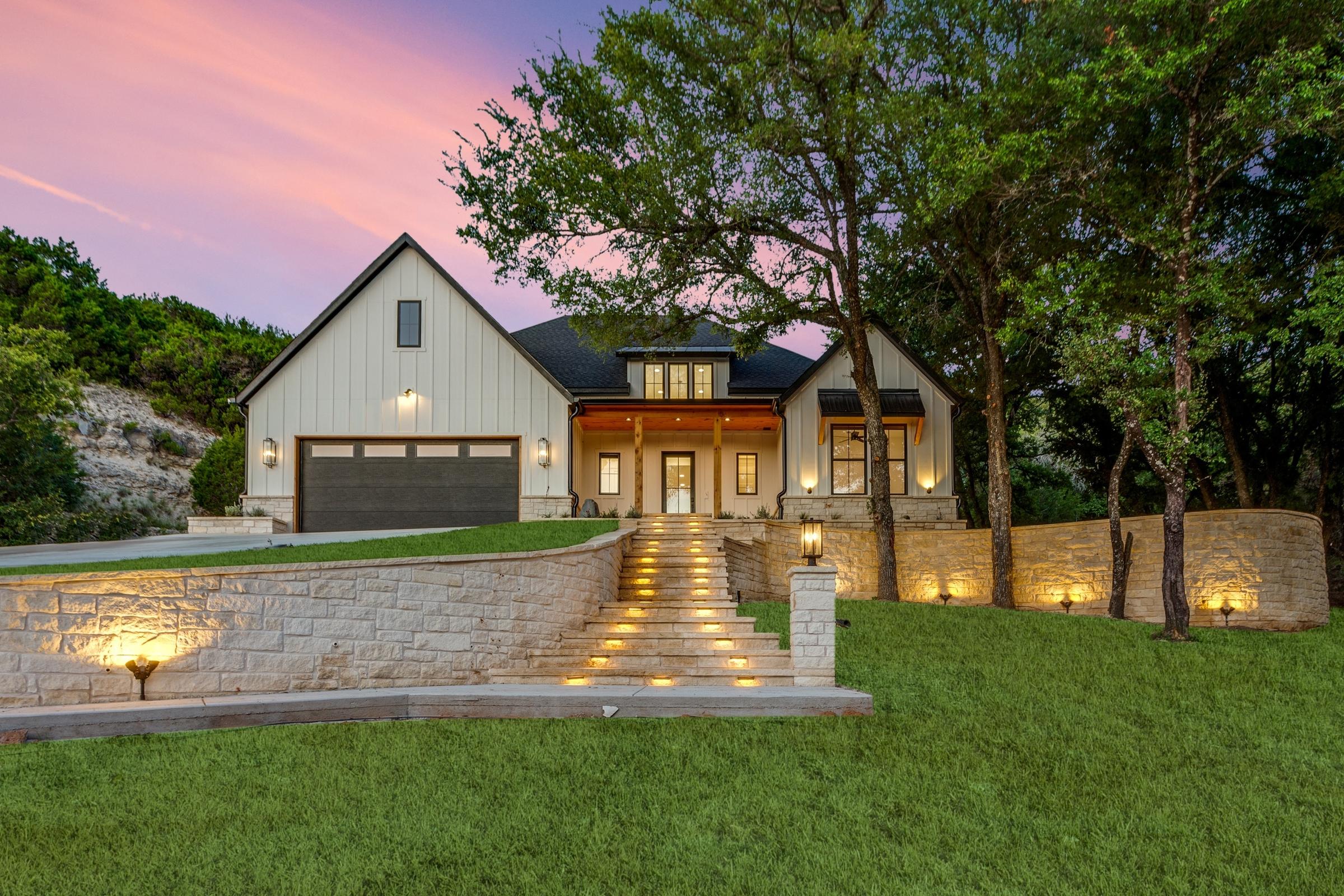 Custom modern farmhouse on hillside with illuminated stone steps, limestone retaining walls, and covered porch at twilight in Cresson, Texas