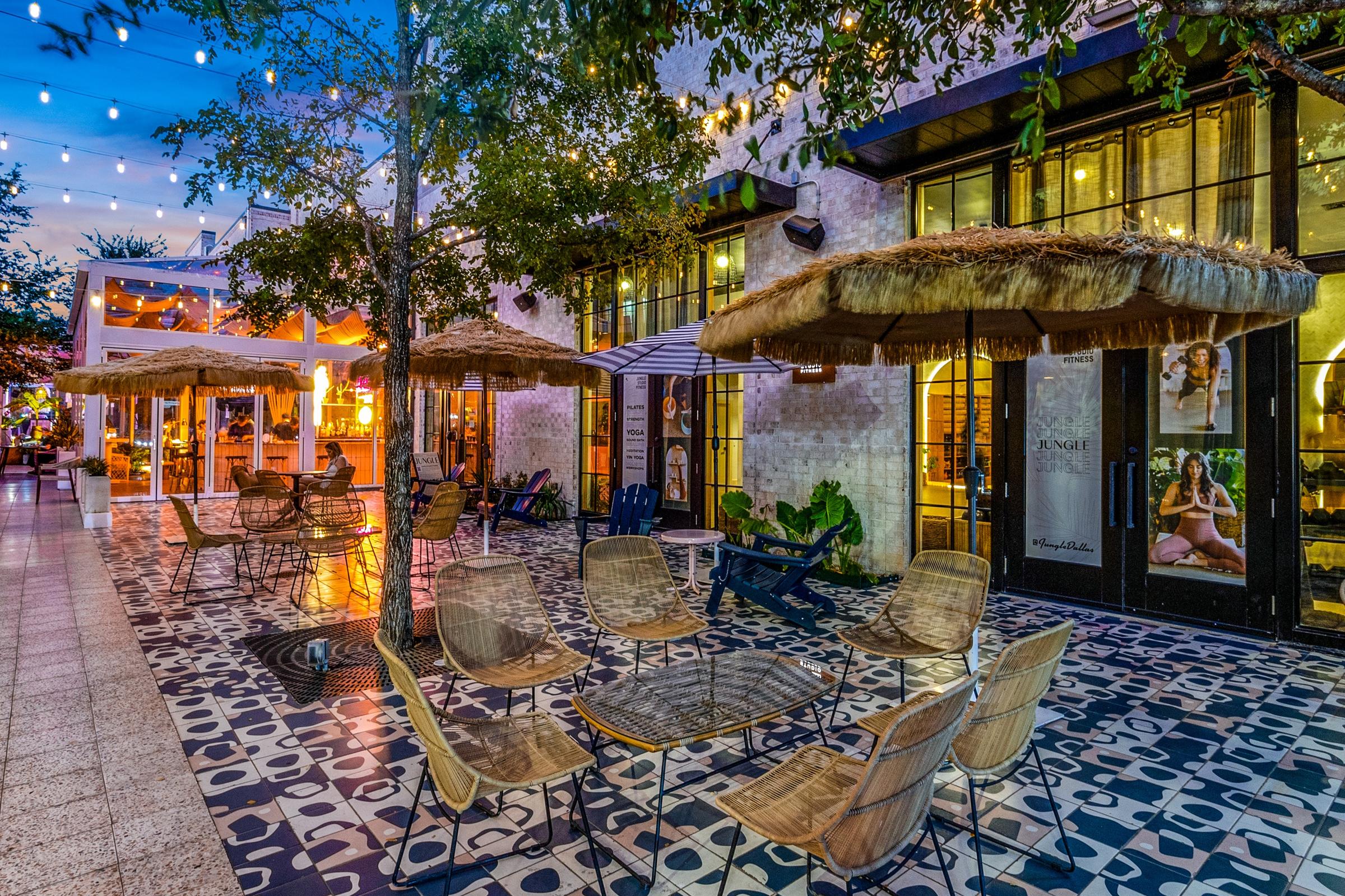Eclectic restaurant outdoor patio with thatched umbrellas, string lights, patterned tile, and warm evening glow at twilight in Dallas, Texas
