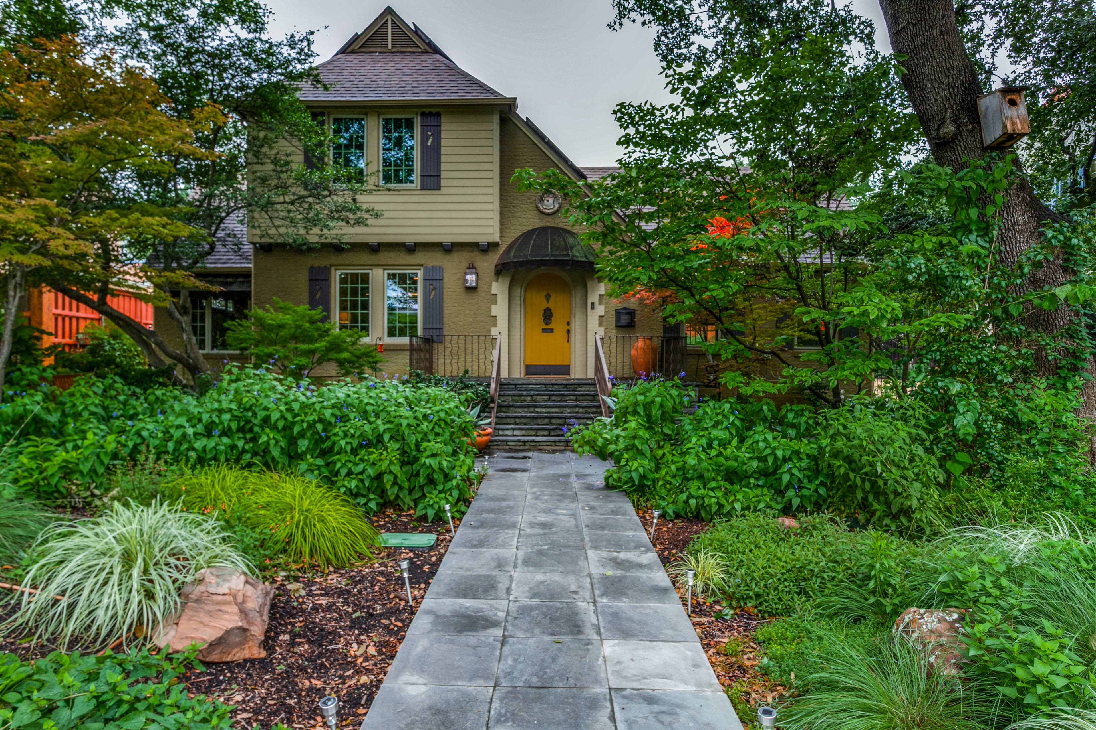 Tudor-style two-story home with olive-green exterior, red front door, and lush landscaping in Dallas, TX