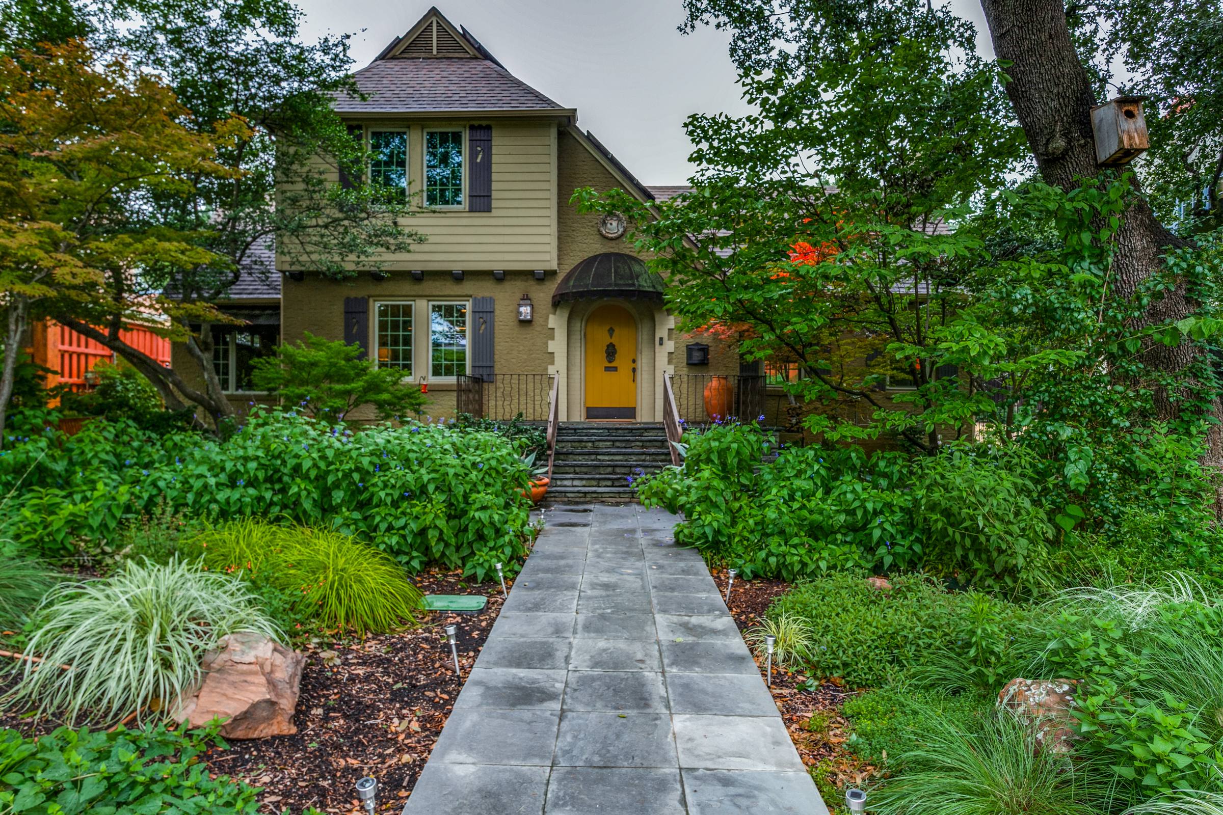Tudor-style two-story home with olive-green exterior, red front door, and lush landscaping in Dallas, TX