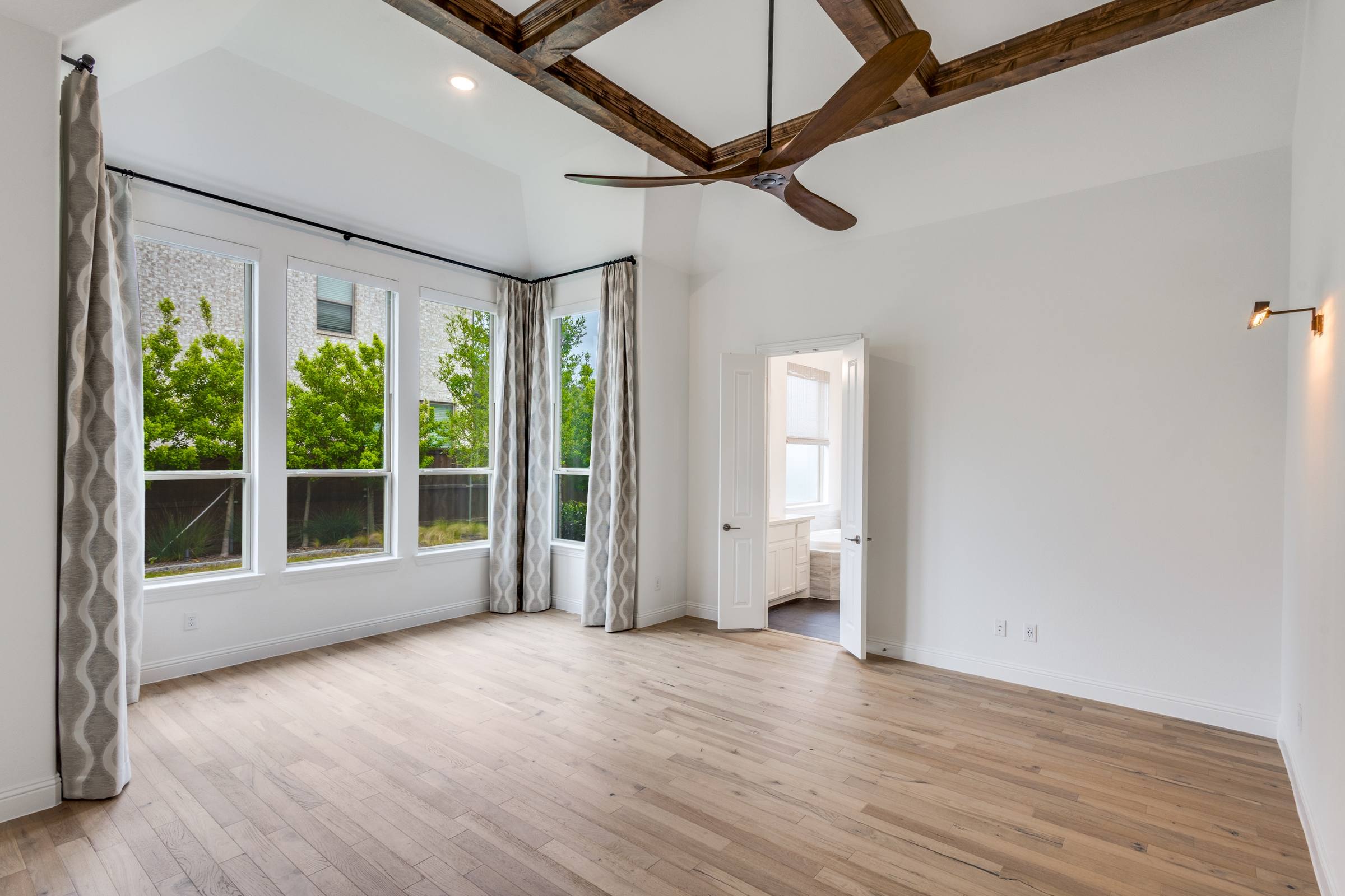 Bright empty living room with wood beam ceiling, hardwood floors and large windows in a Celina, Texas single-family home