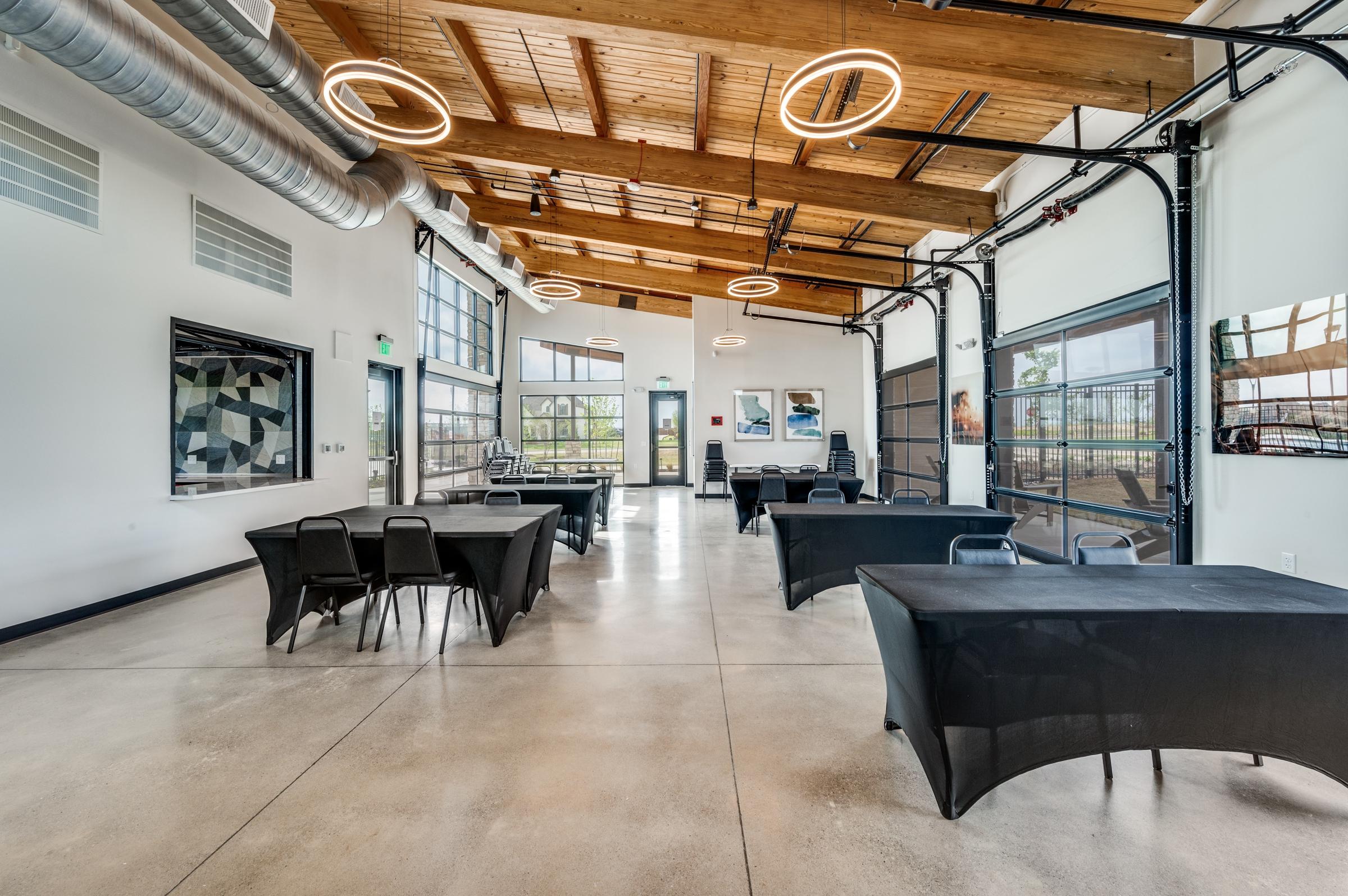 Modern commercial event space with wood beam ceiling, polished concrete floors, garage doors, and industrial lighting in Oak Point, Texas