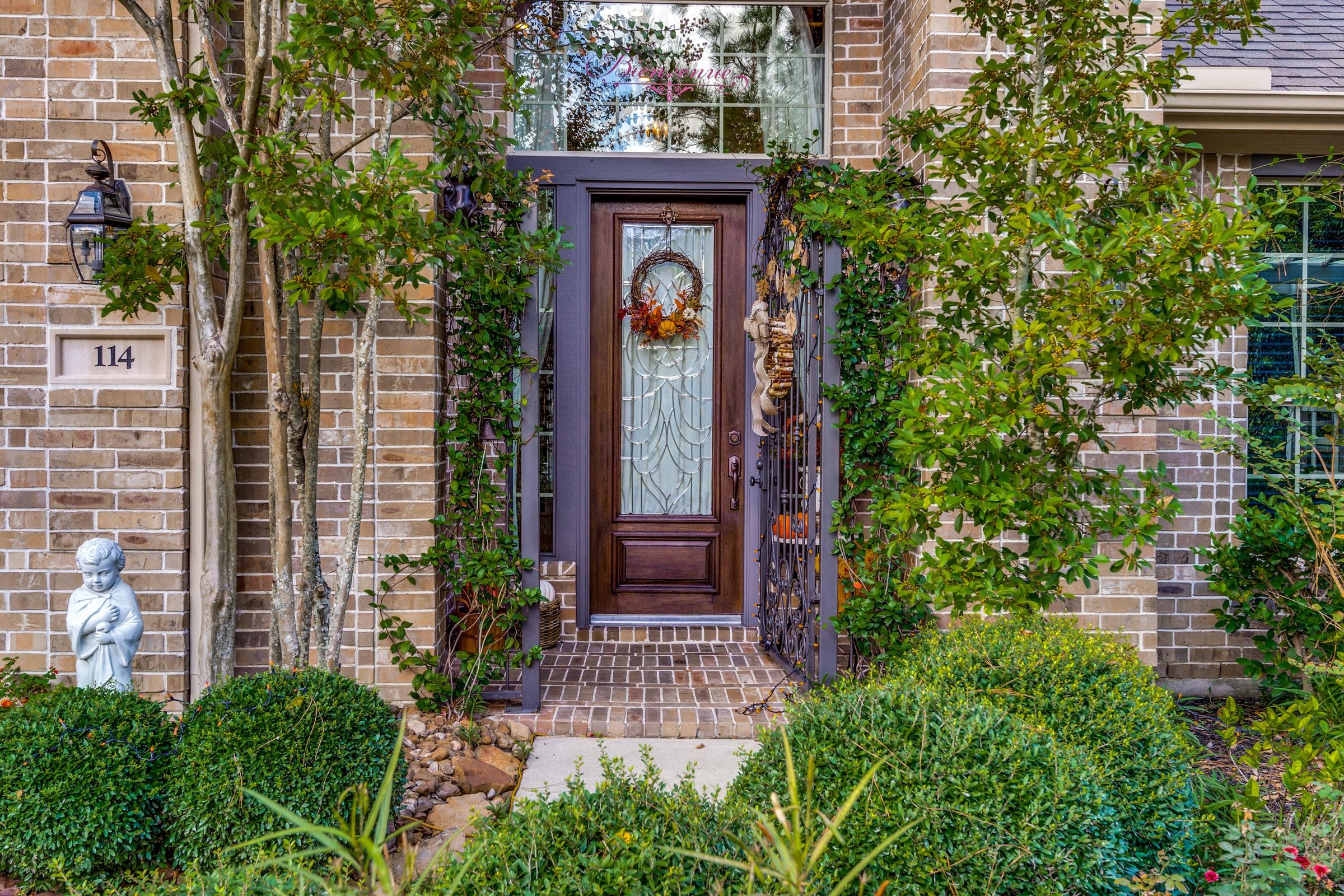 Charming brick home front entry with ornate glass door, climbing ivy, and lush landscaping in Palo Pinto, Texas