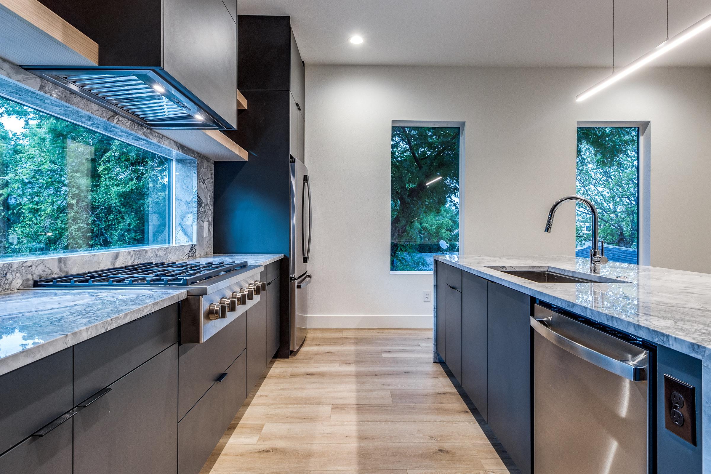 Modern kitchen with dark cabinetry, marble countertops, stainless steel appliances, and hardwood floors in a Dallas, Texas rental property