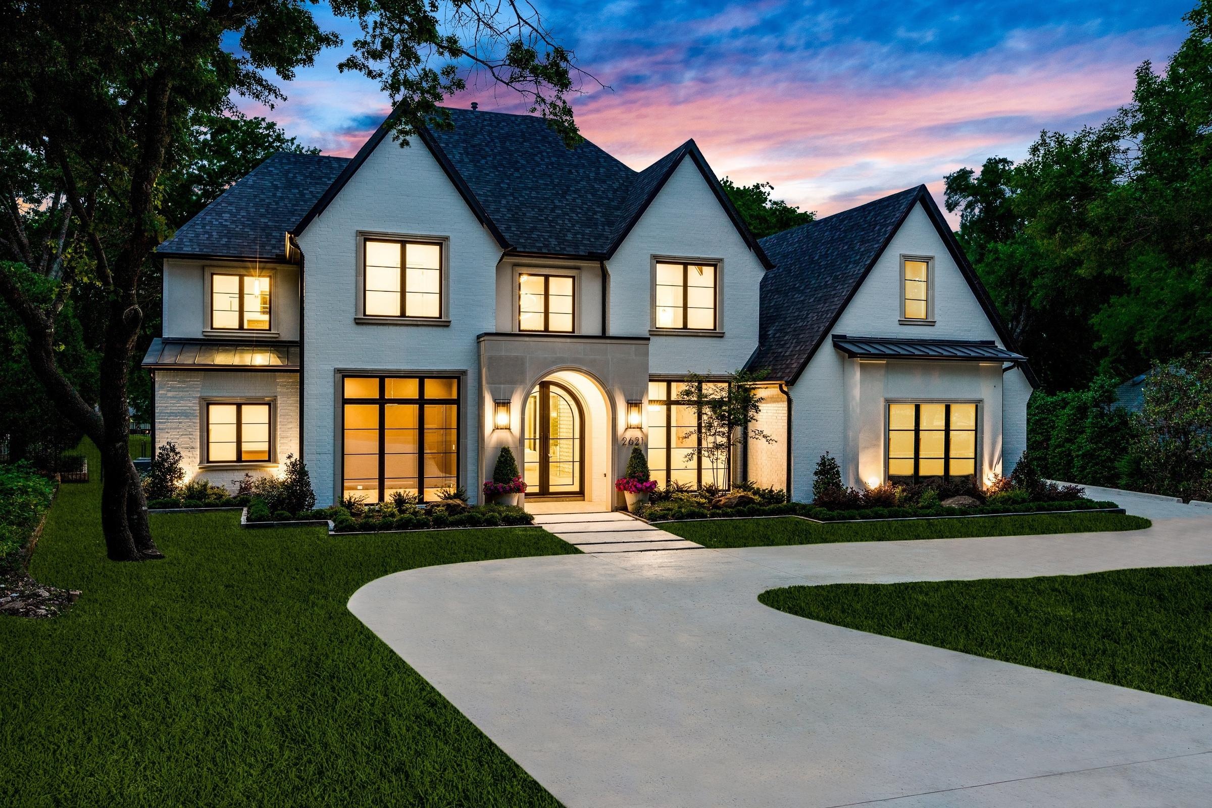 White painted brick luxury custom home with arched entry, circular driveway, and landscape lighting at twilight in McKinney, Texas