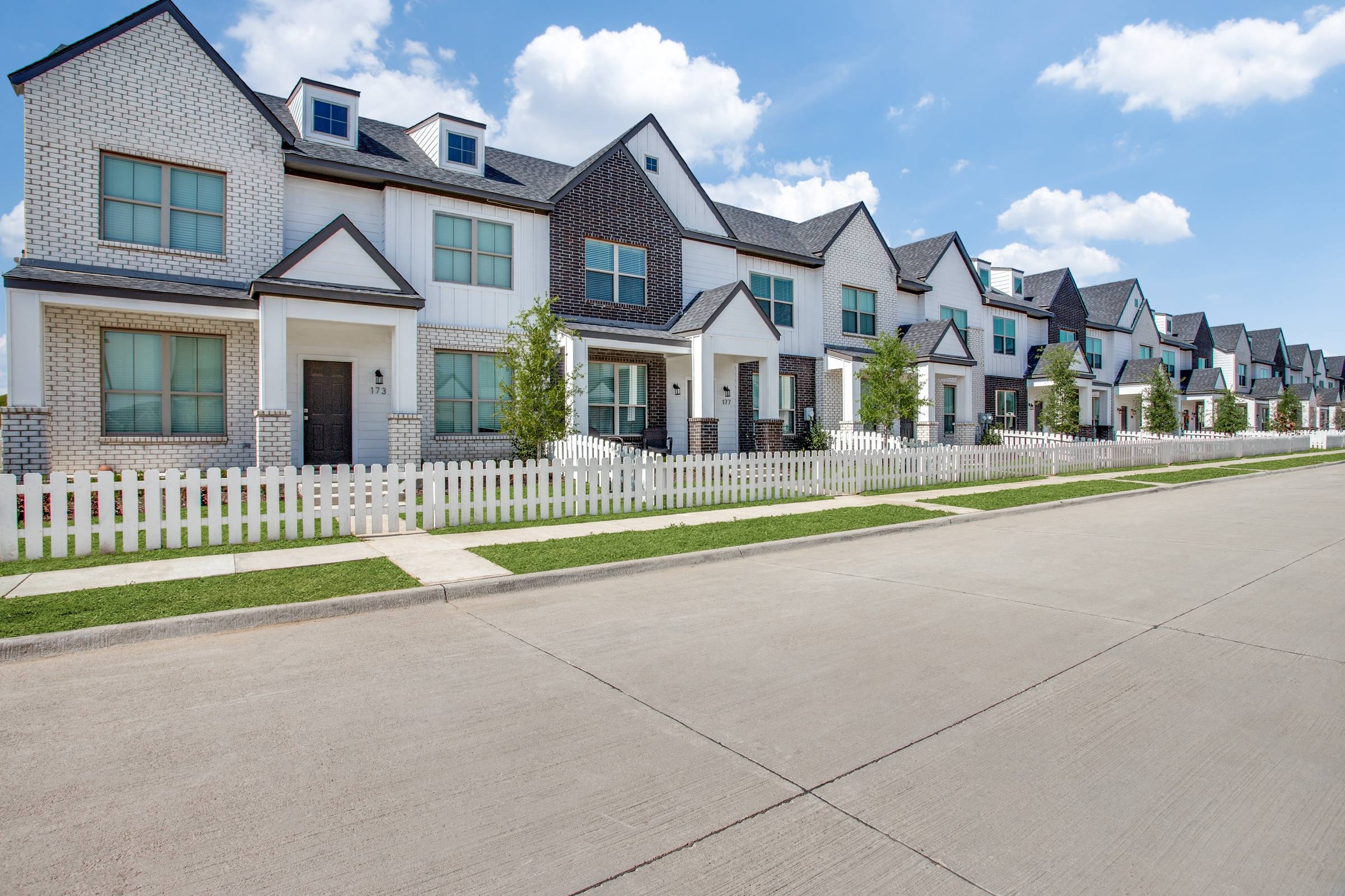 Row of modern new-build townhomes with white picket fences and mixed brick and board-and-batten siding in Waxahachie, Texas