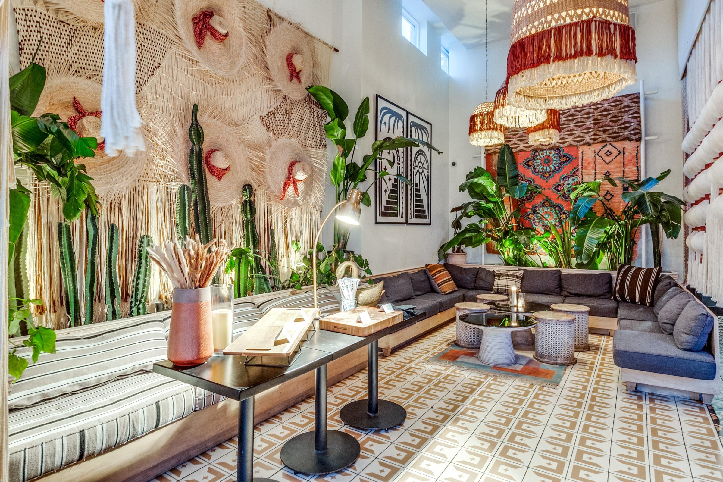 Stylish restaurant private room with bohemian wall tapestry, tropical plants, sectional seating, and layered pendant lighting in Dallas, Texas