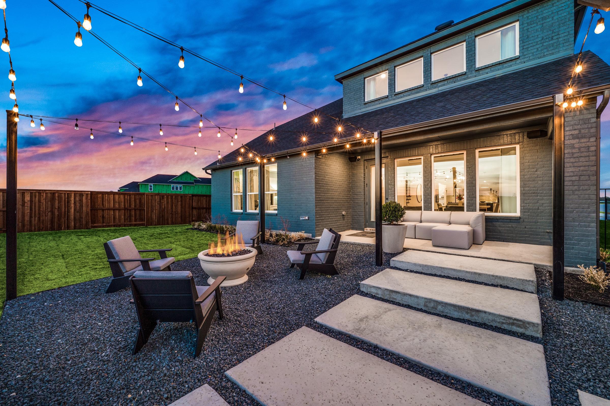 Modern backyard at twilight with fire pit seating area, string lights, covered patio, and sunset sky in Prosper, Texas