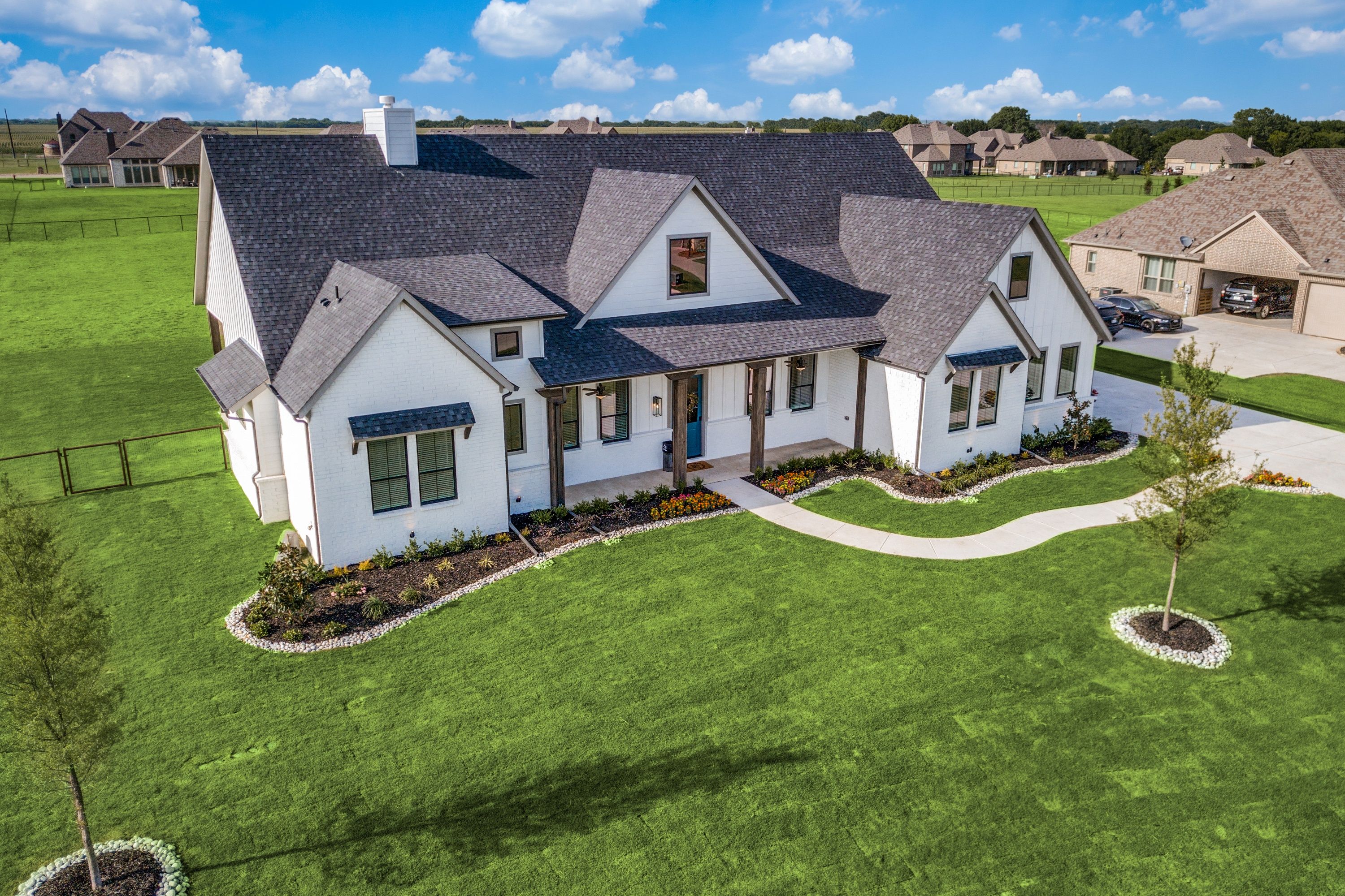 Aerial drone view of a white modern farmhouse custom home with manicured landscaping and green lawn on a large lot in Van Alstyne, Texas