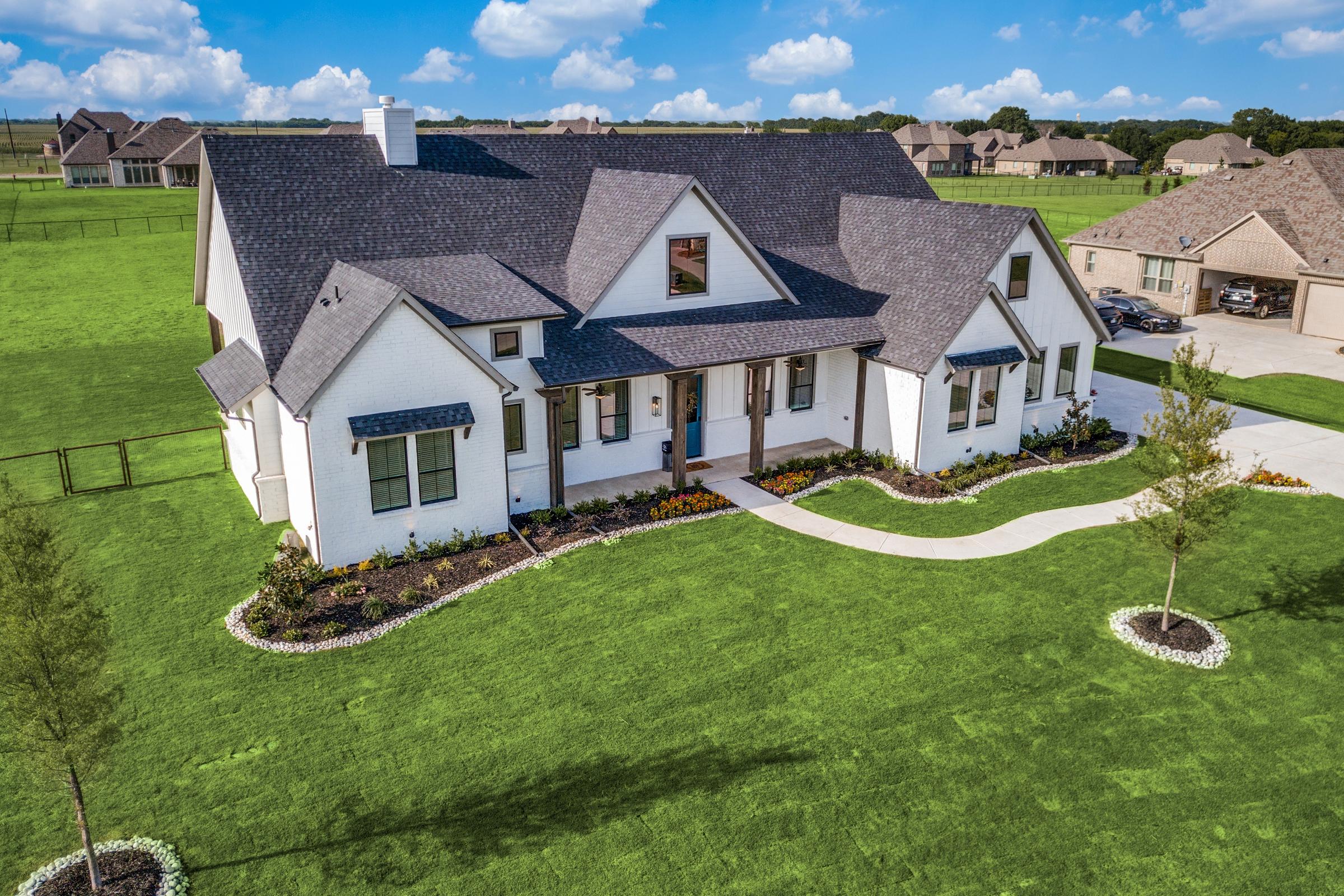 Aerial drone view of a white modern farmhouse custom home with manicured landscaping and green lawn on a large lot in Van Alstyne, Texas