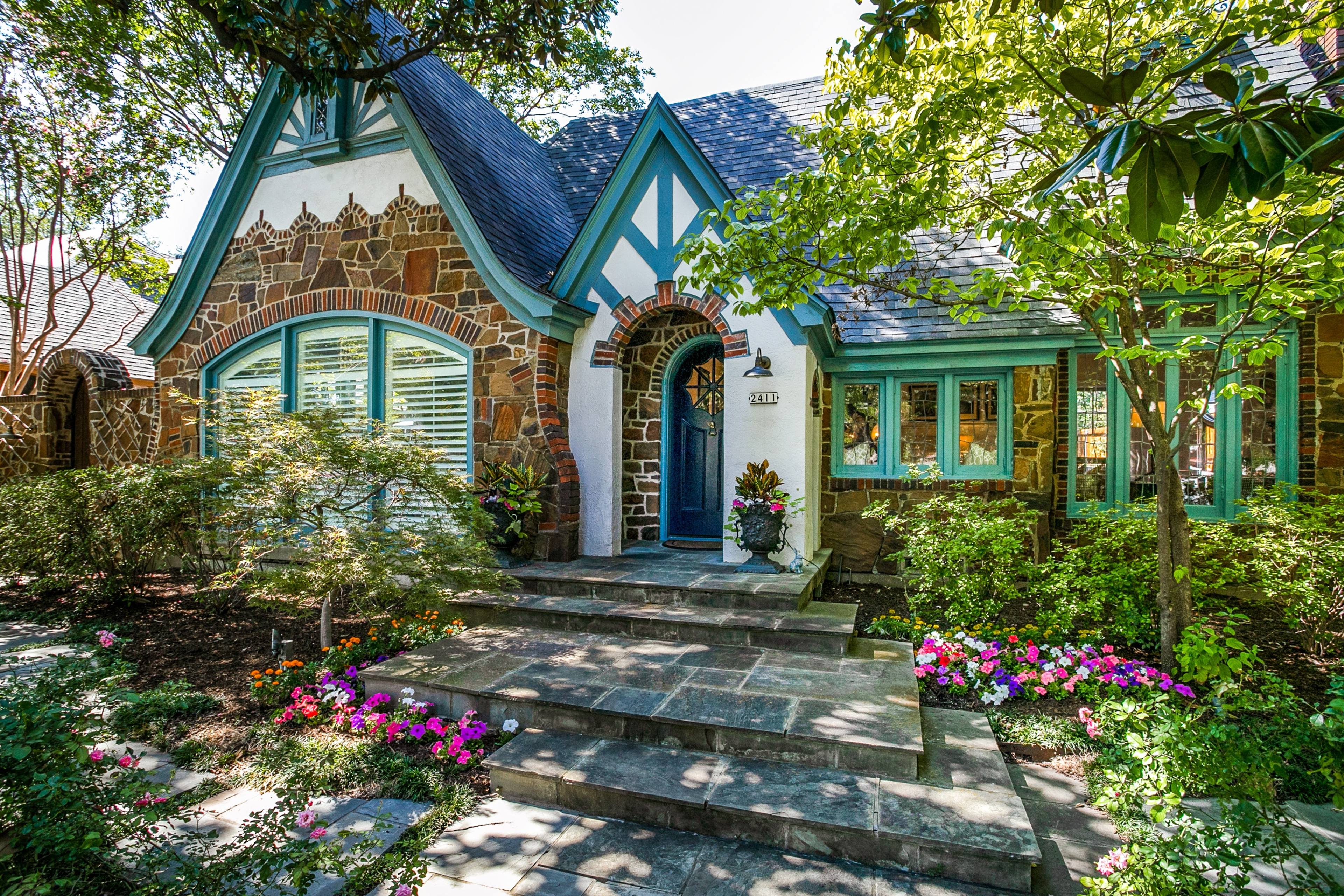 Charming Tudor-style stone cottage with teal trim, arched front door, and flowering landscaping in Dallas, Texas