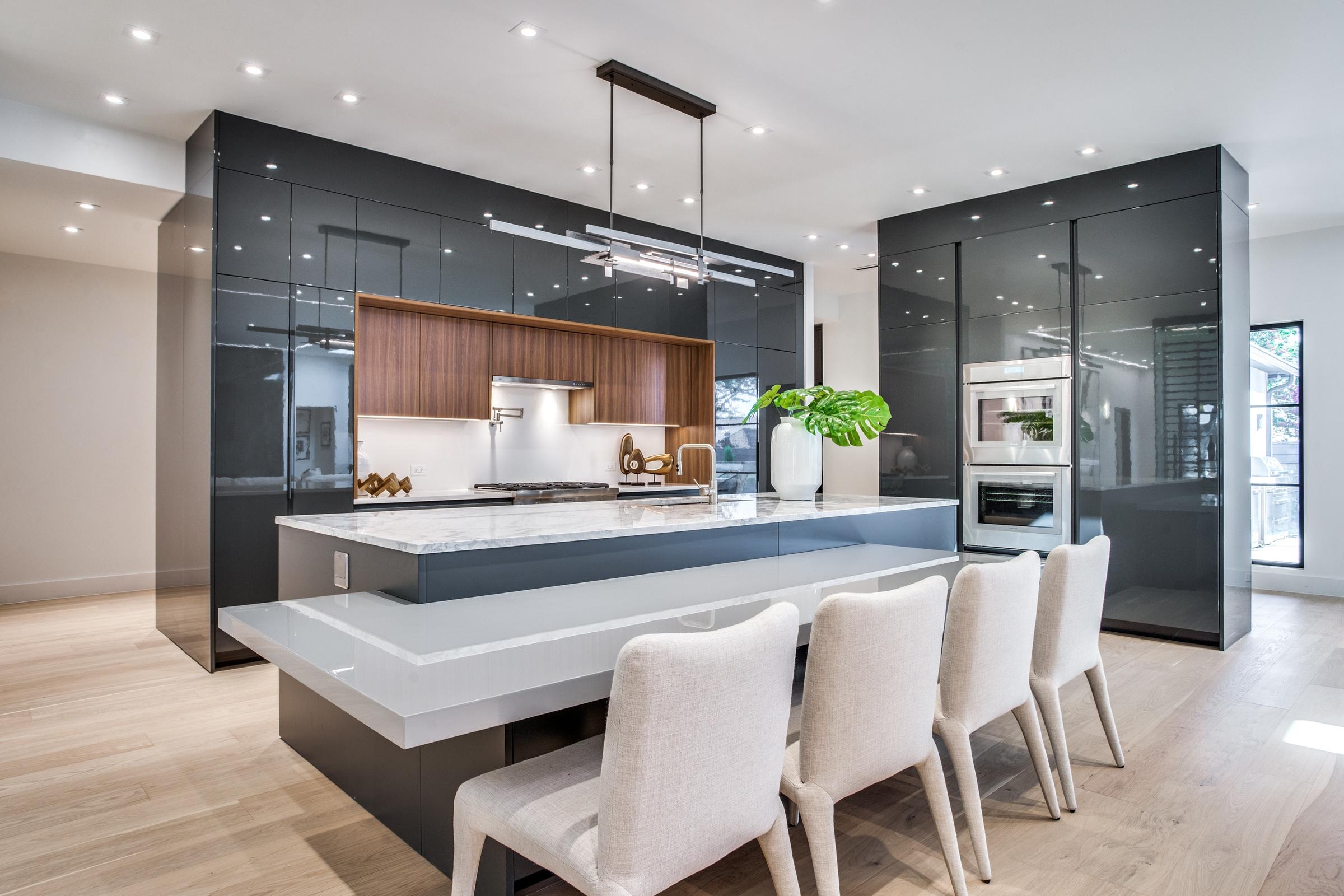 Modern kitchen with dark gloss cabinetry, marble waterfall island, breakfast bar seating, and walnut wood backsplash in a Dallas, Texas custom home