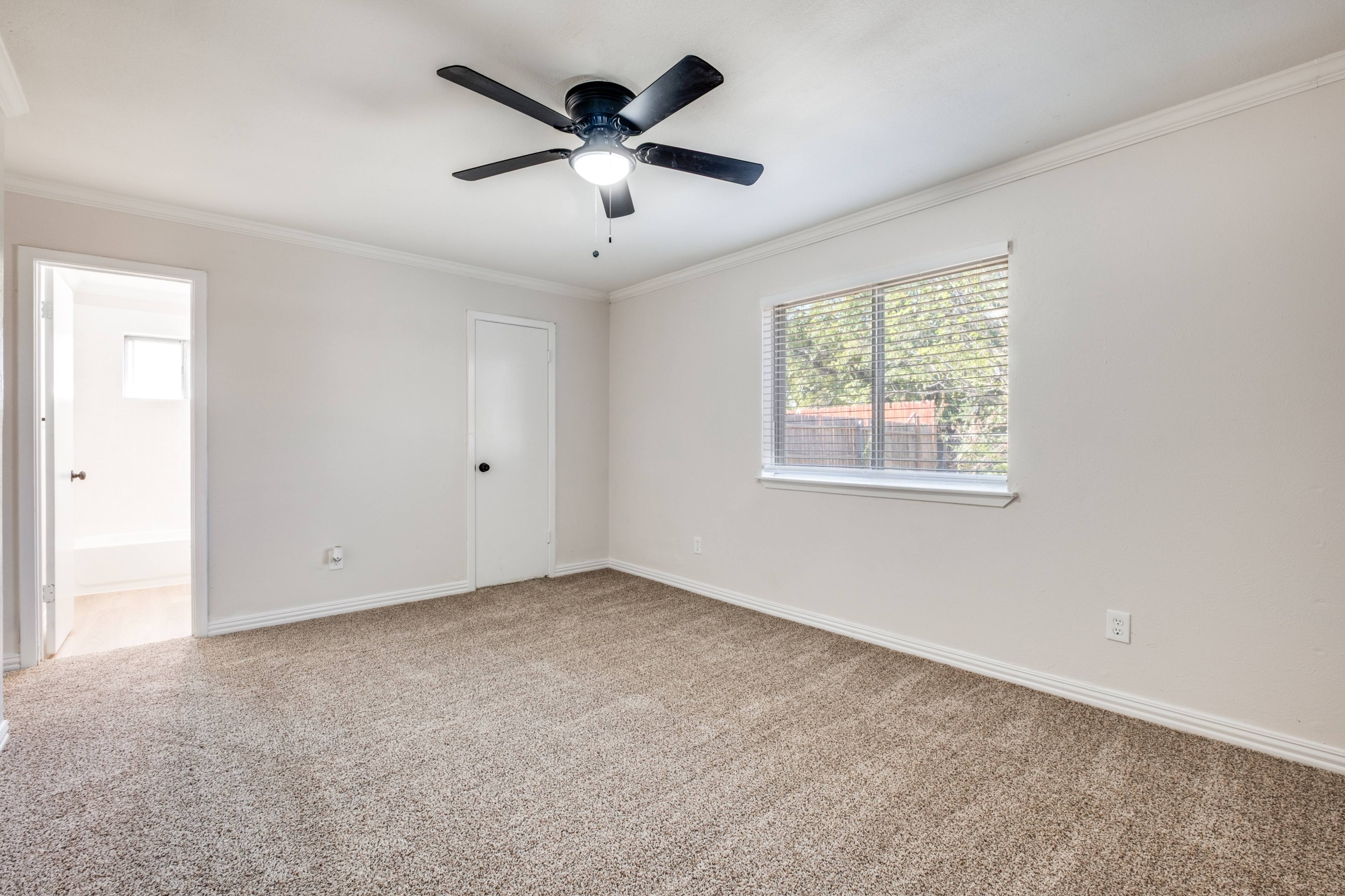Empty bedroom with carpet, ceiling fan, and window before virtual staging in Mesquite, Texas