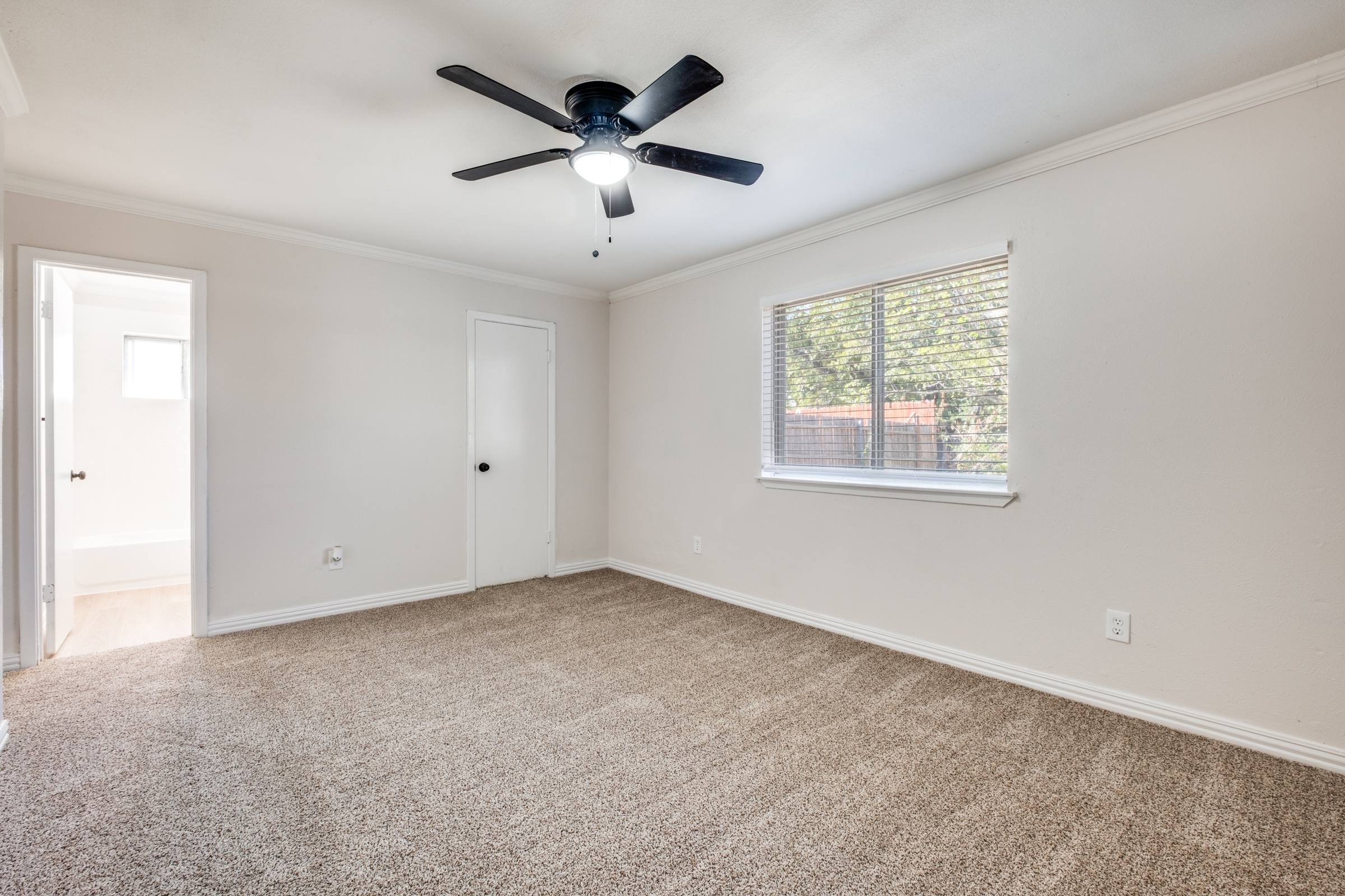 Empty bedroom with carpet, ceiling fan, and window before virtual staging in Mesquite, Texas