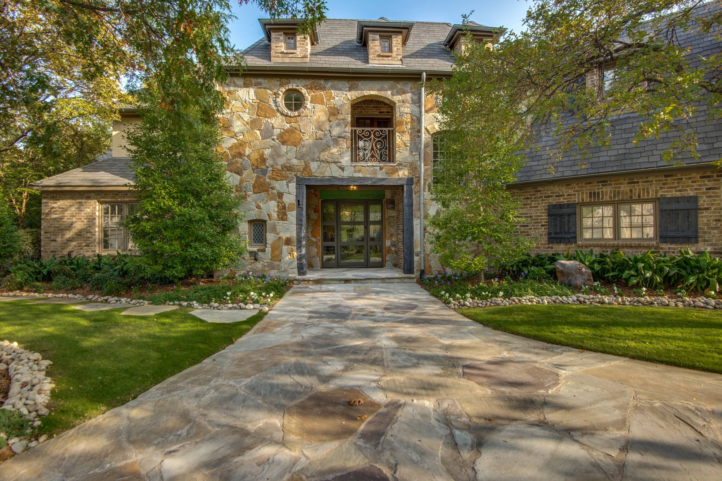 Professional front exterior photograph of stone facade luxury home with flagstone walkway, manicured lawn, and mature trees in Frisco, Texas