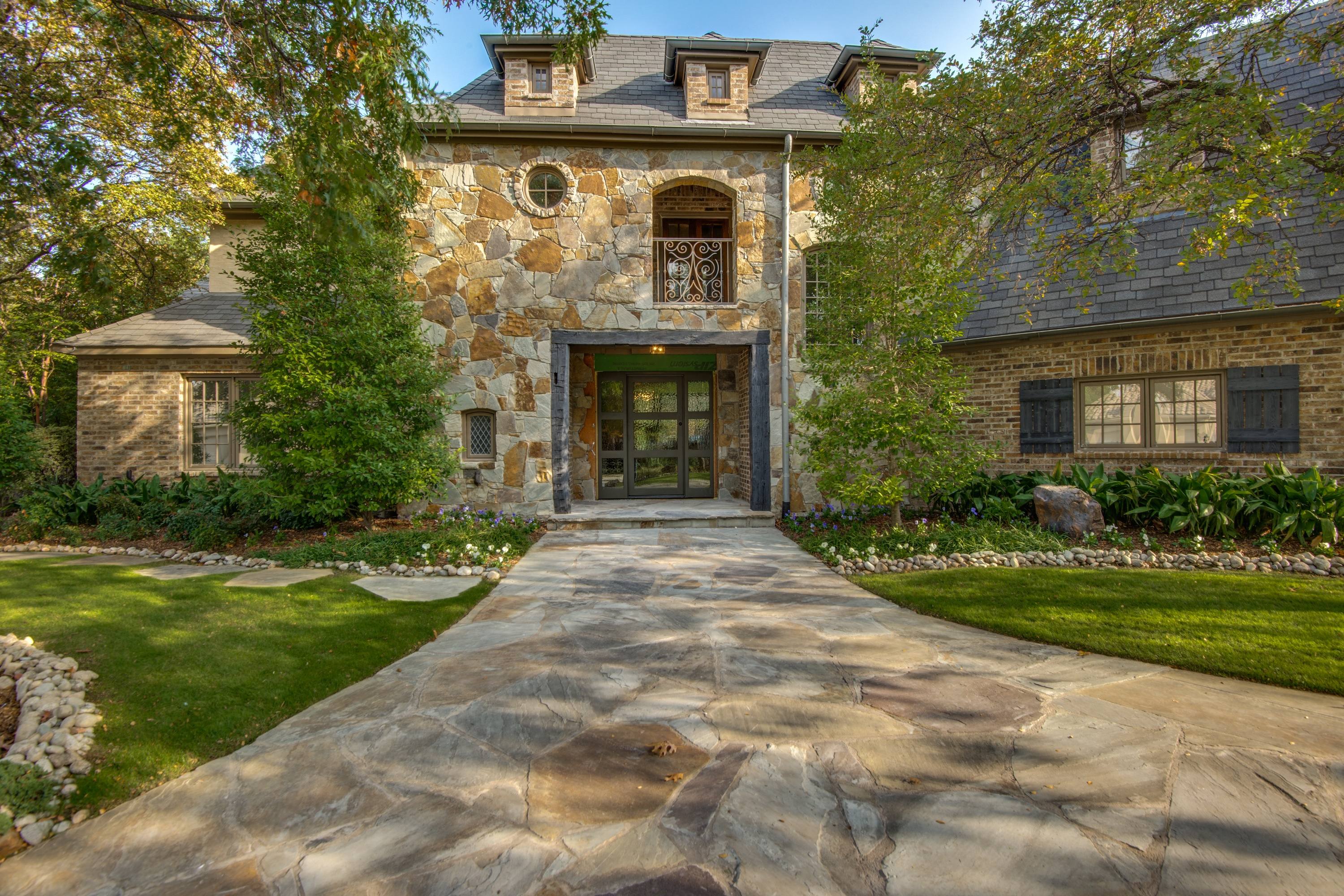 Professional front exterior photograph of stone facade luxury home with flagstone walkway, manicured lawn, and mature trees in Frisco, Texas