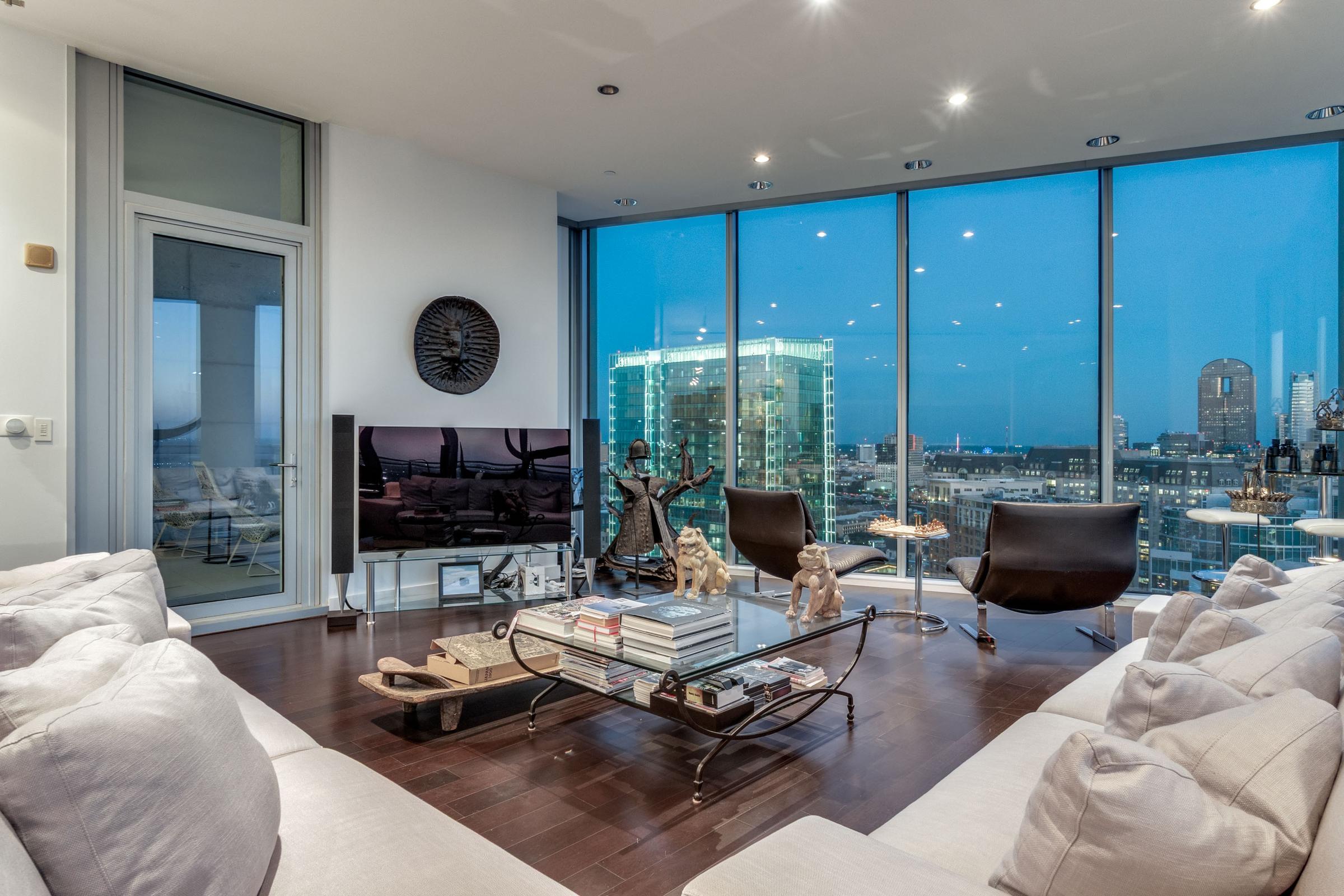 High-rise living room at twilight with panoramic downtown Dallas skyline views through floor-to-ceiling windows in Dallas, Texas