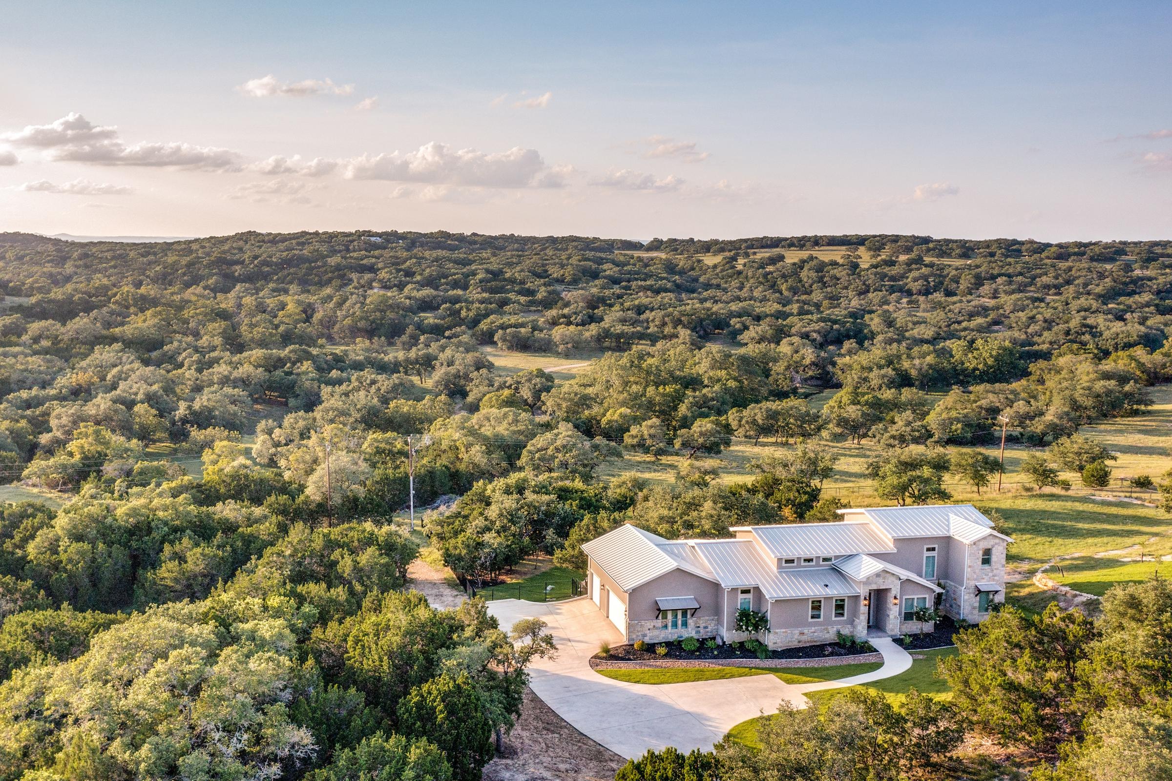 Aerial view of a modern ranch-style home nestled in Texas Hill Country oak trees near Canyon Lake