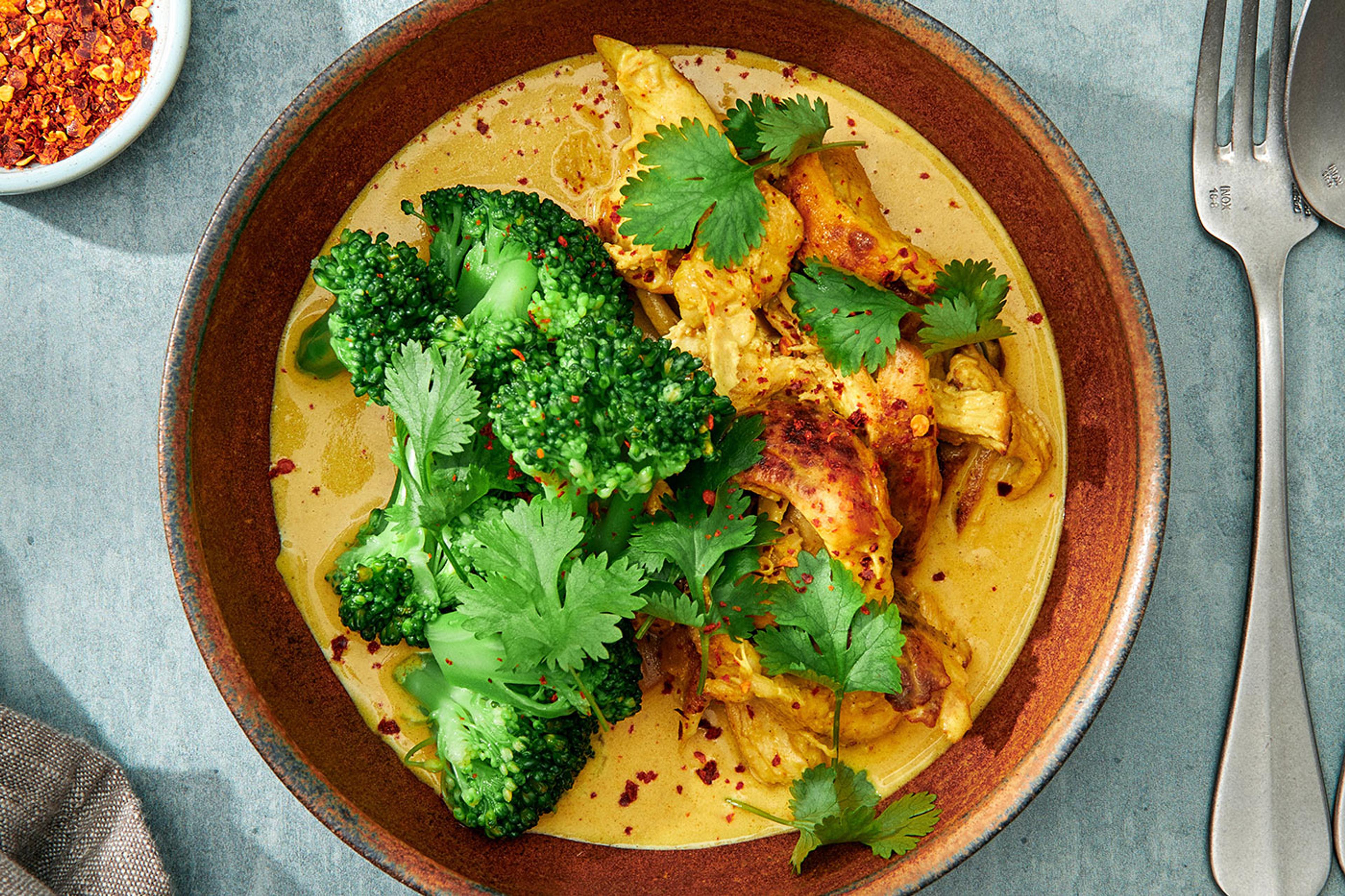 En djup tallrik med en gul kycklingcurry toppad med broccoli