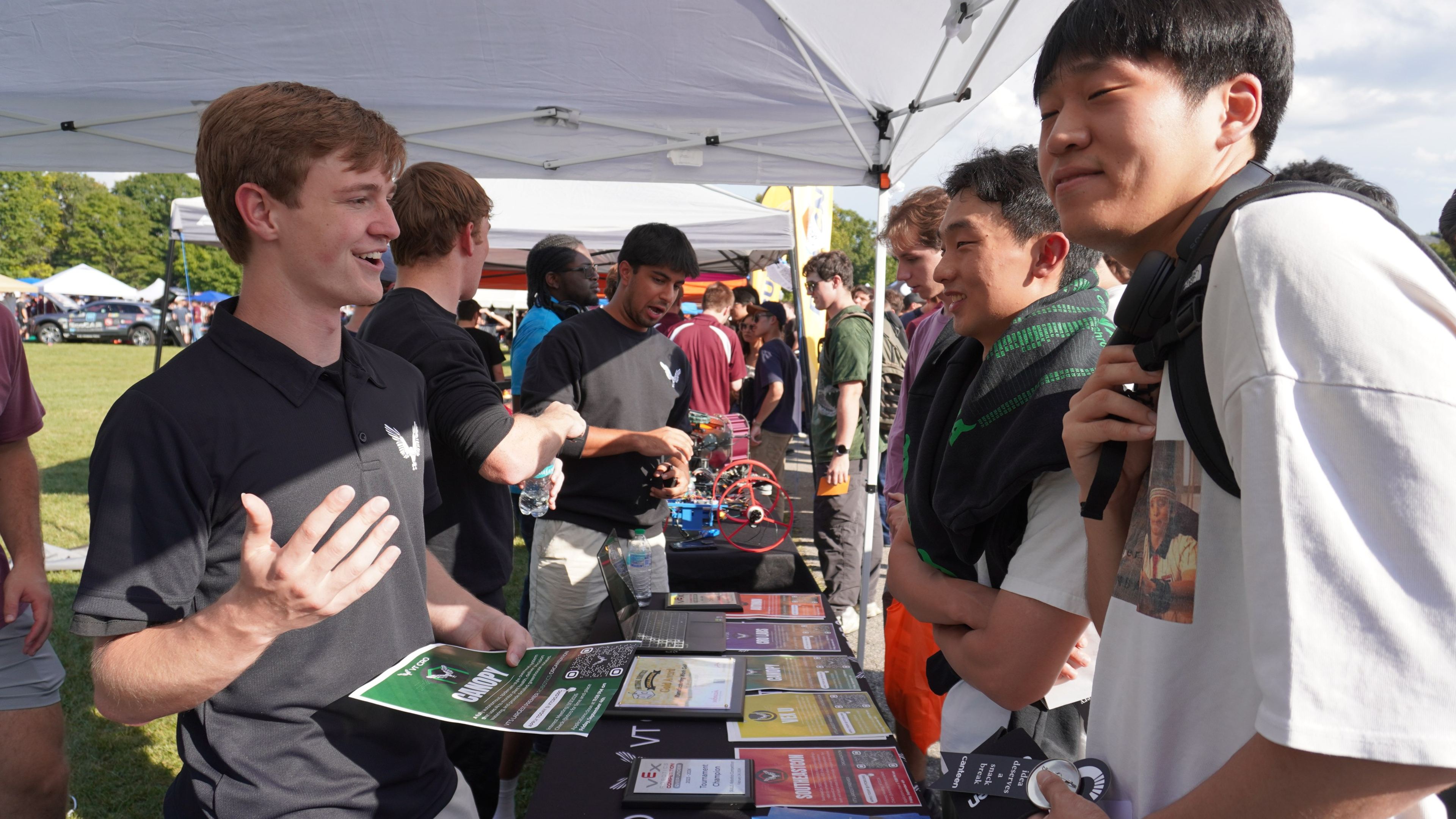 A member explaining the design teams to students at the tent