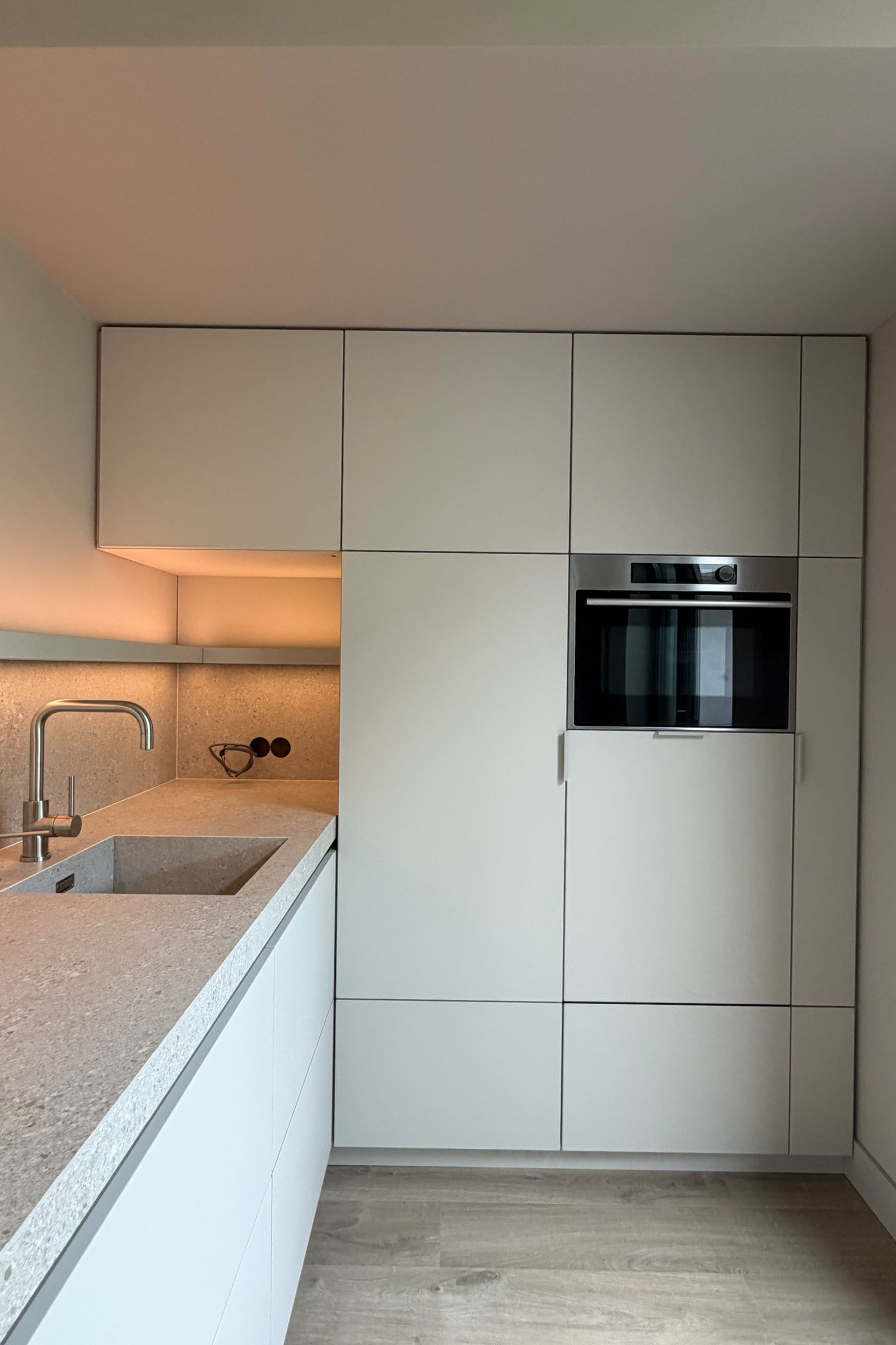 Hoge lichtgrijze kasten met ingebouwde oven naast het werkblad in terrazzolook met spoelbak en rvs kraan