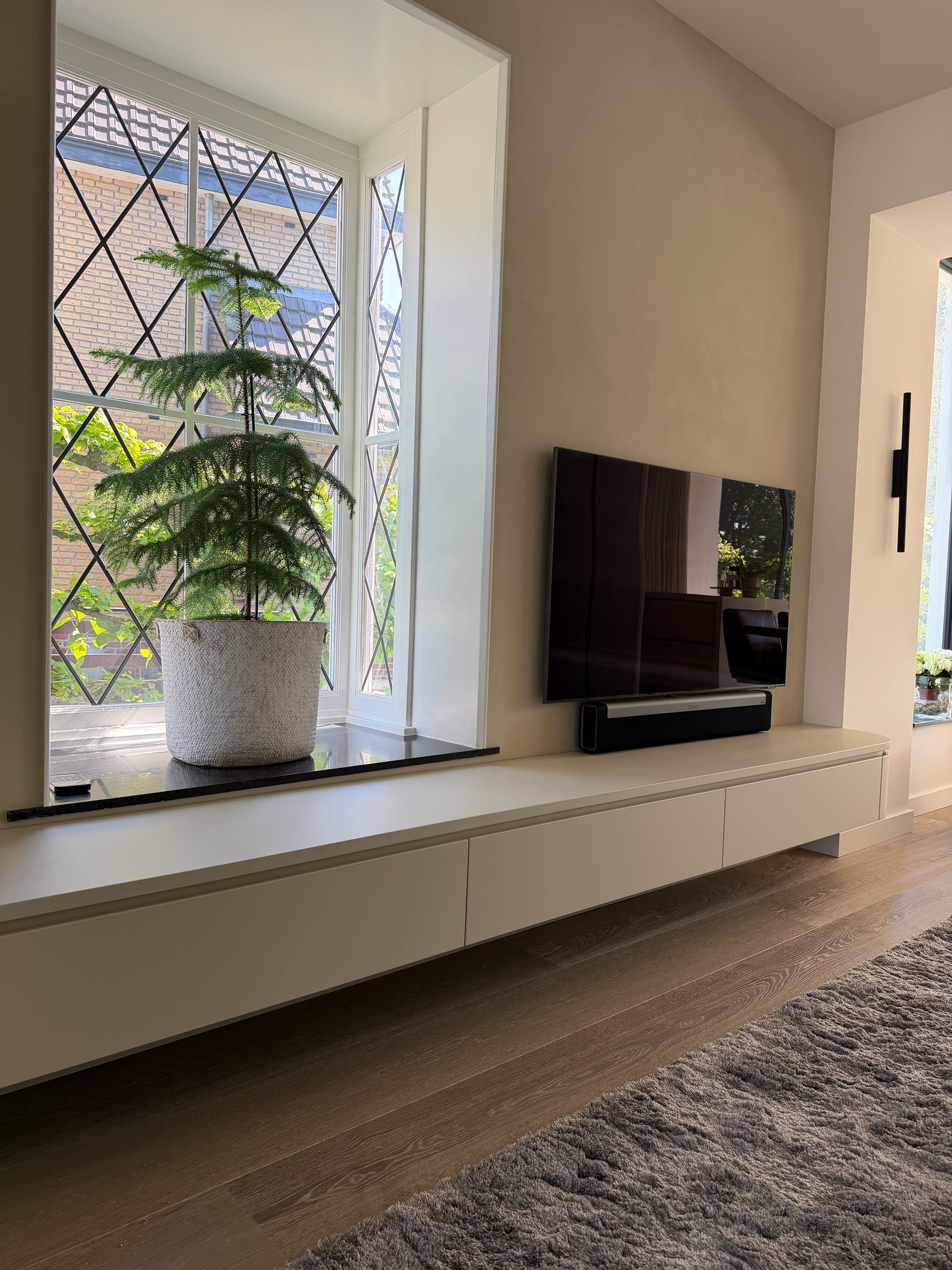 Lang zwevend tv-meubel in gebroken wit met greeploze lades, doorlopend onder een raam met glas-in-lood