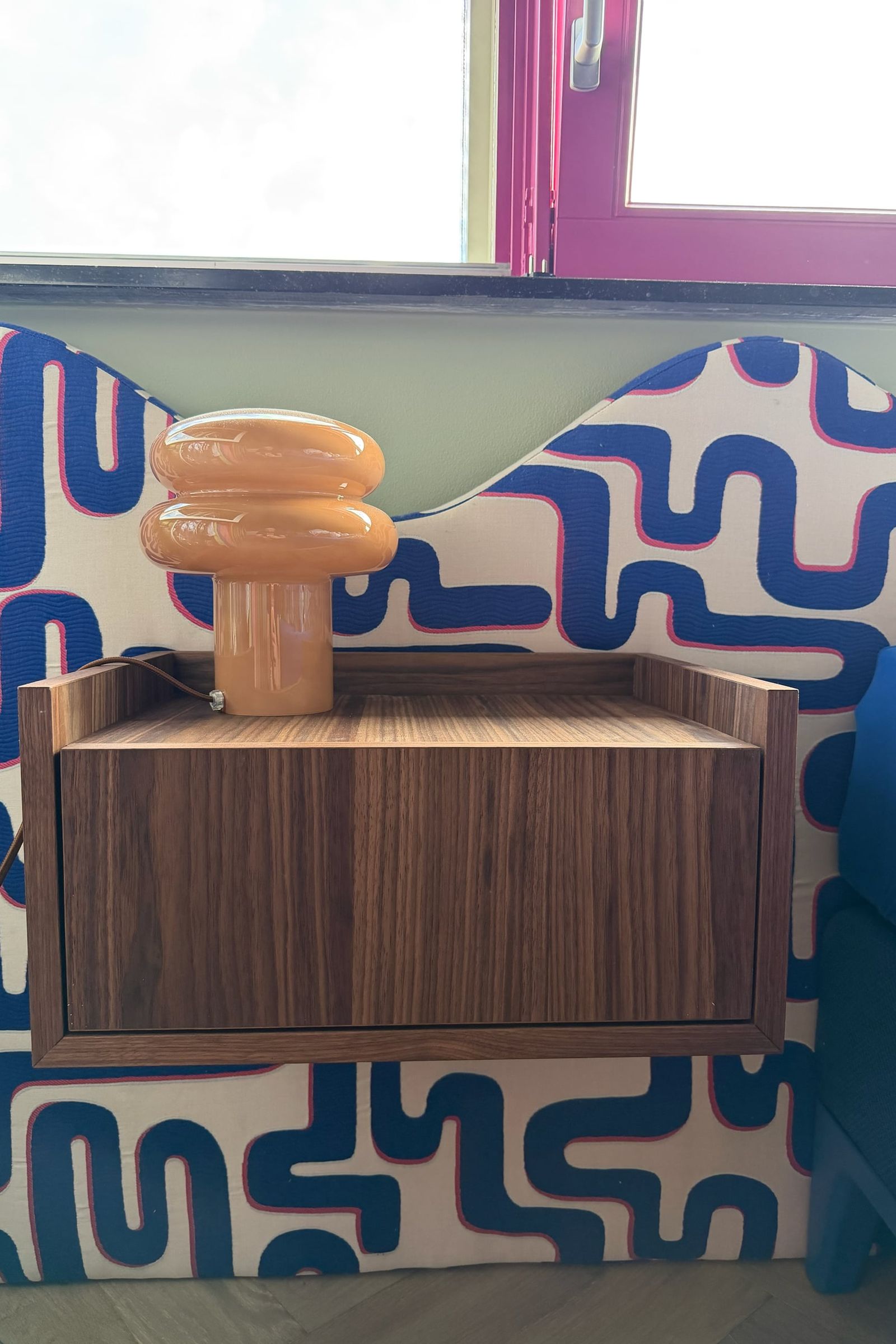 Zwevend nachtkastje in walnoot met lade en oranje lamp, tegen een golvend hoofdbord met blauw patroon