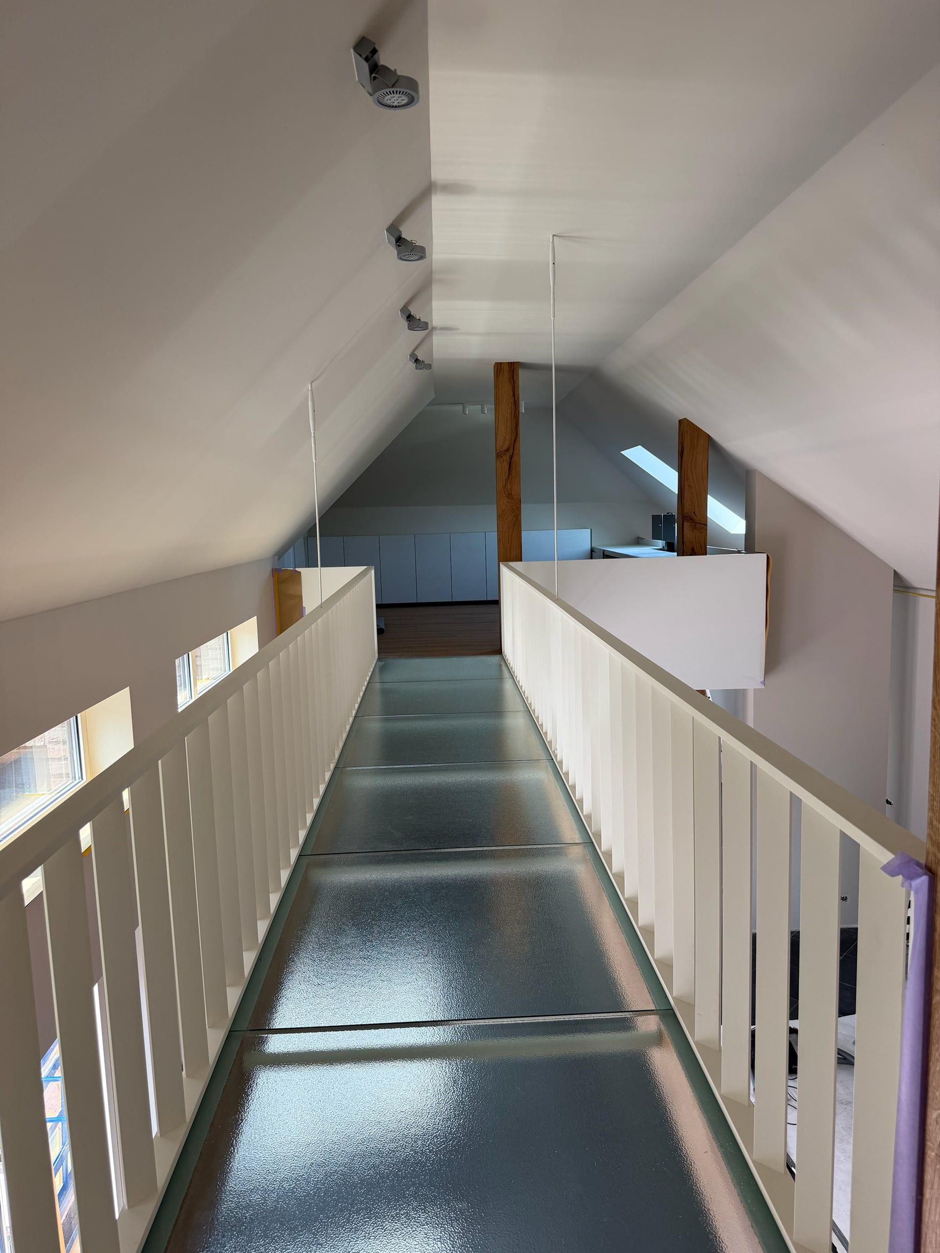 Loopbrug met vloer van structuurglas tussen witte spijlenbalustrades, met eiken staanders onder de schuine kap
