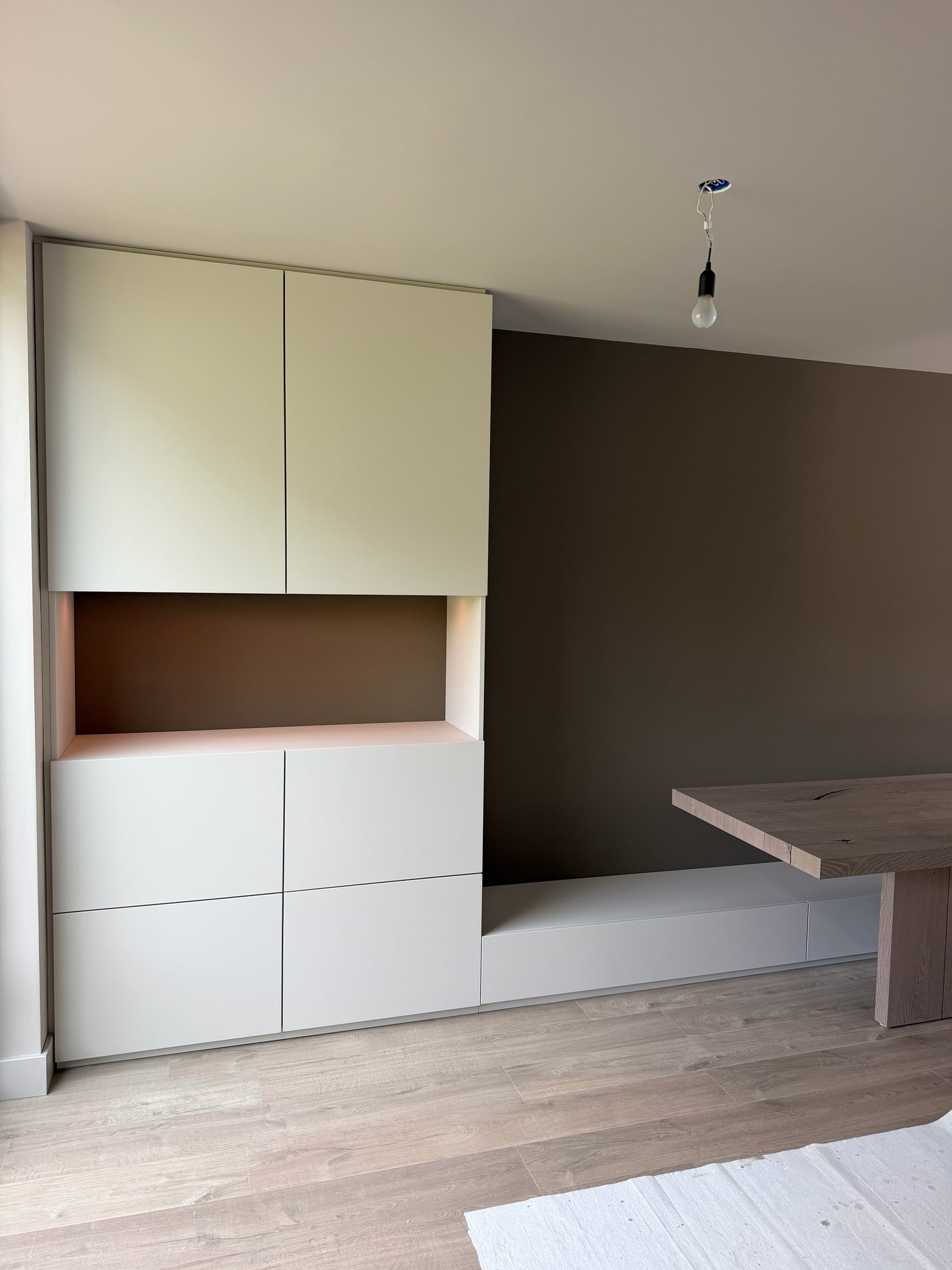 Kastenwand met greeploze lichte fronten en verlichte nis, doorlopend in een lage bank met laden