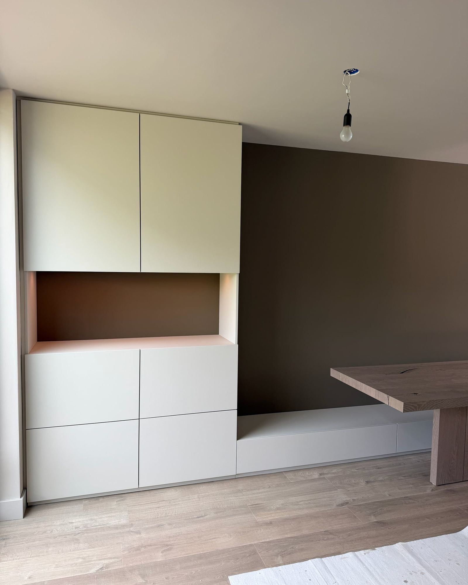 Kastenwand met greeploze lichte fronten en verlichte nis, doorlopend in een lage bank met laden
