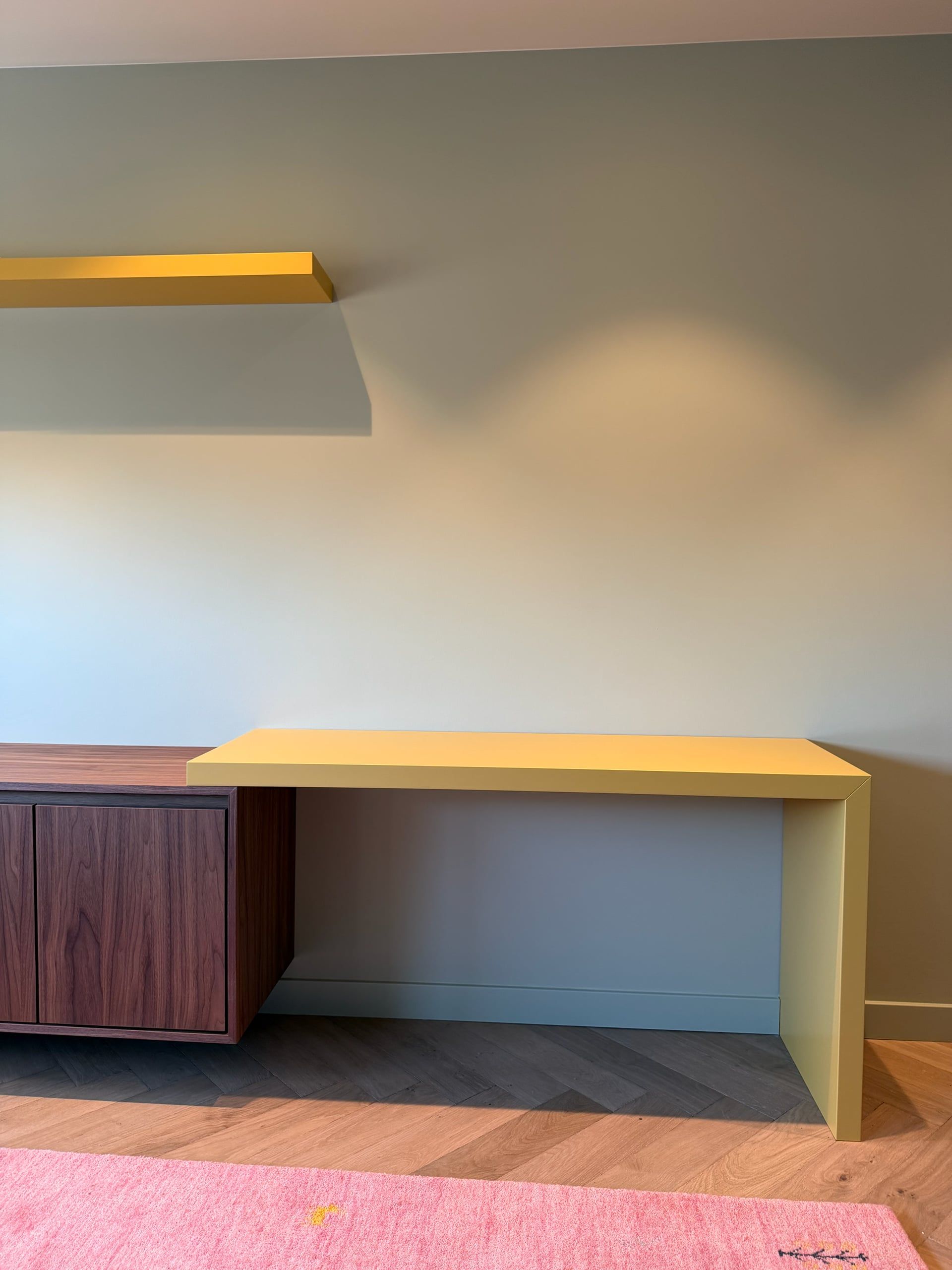 Geel bureau met een schuine zijwang, aansluitend op een zwevend dressoir in walnoot