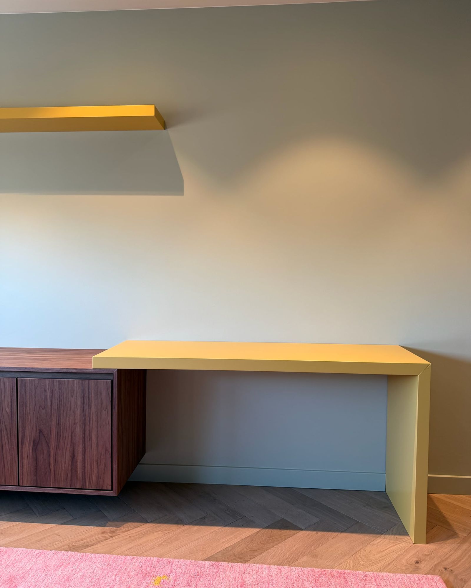 Geel bureau met een schuine zijwang, aansluitend op een zwevend dressoir in walnoot