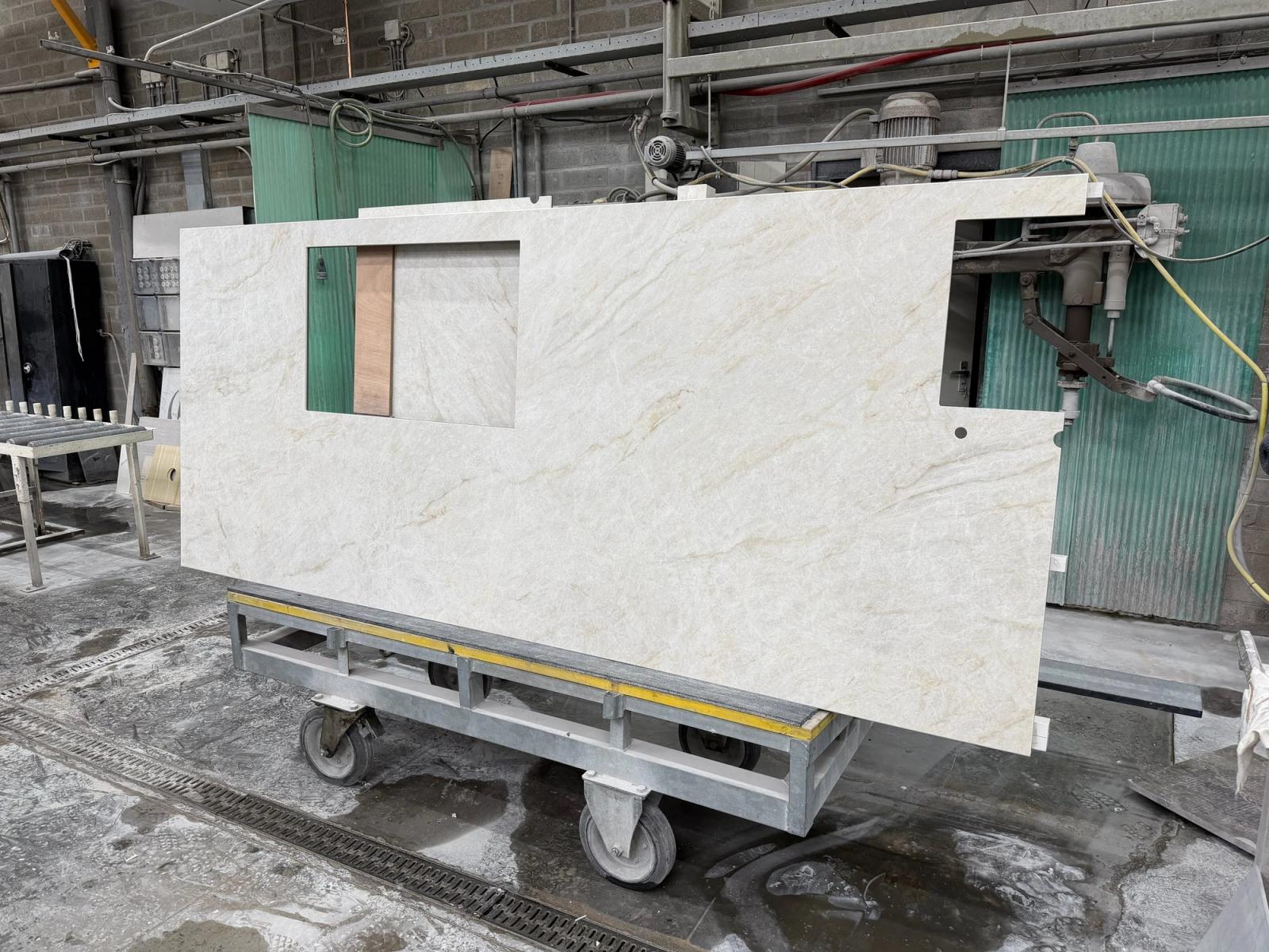 Werkblad van lichte steen met uitsparingen, rechtop op een transportkar in een steenwerkplaats