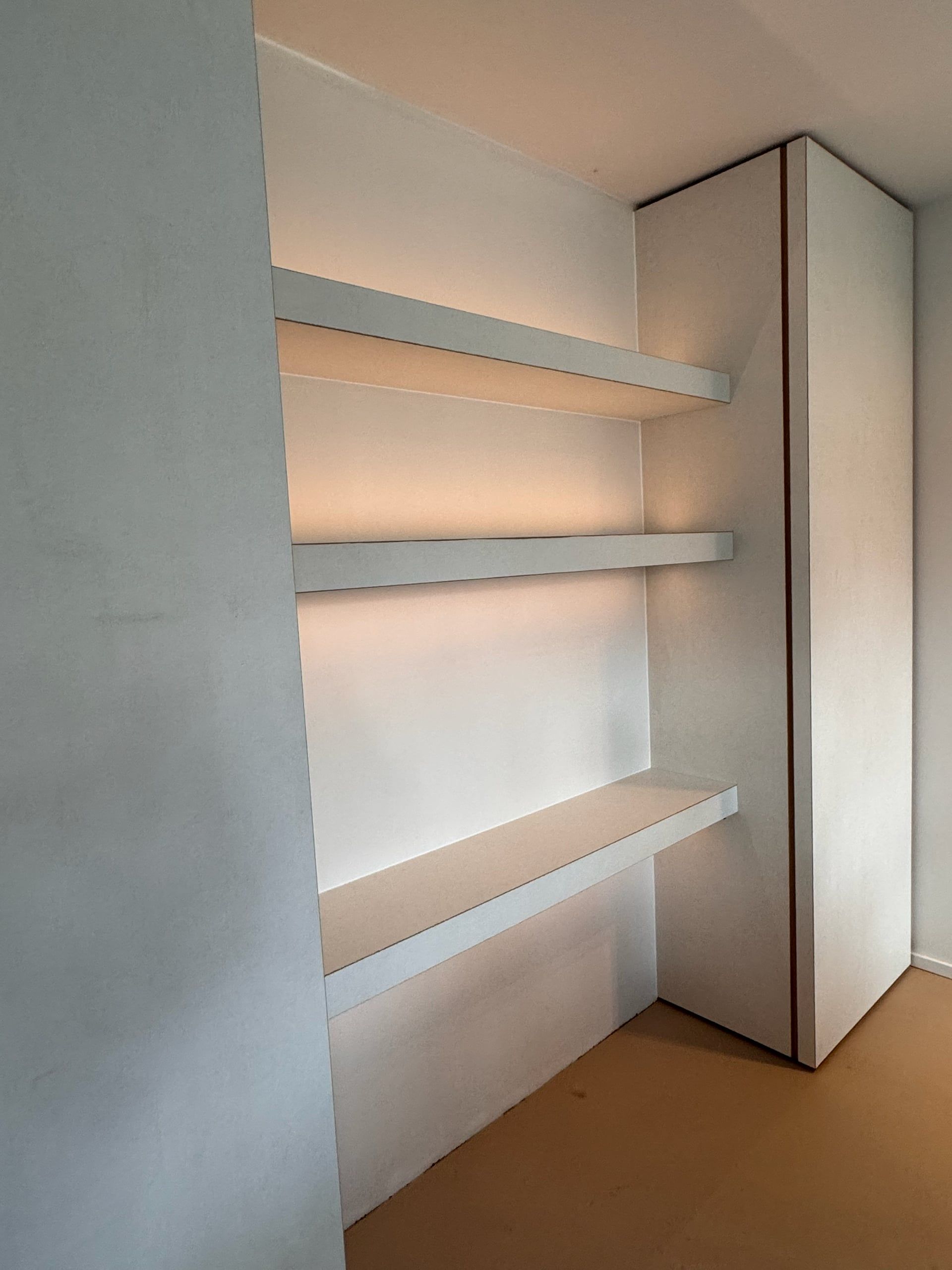 Drie dikke witte zwevende planken met warme ledverlichting eronder in een nis naast een hoge witte kolomkast