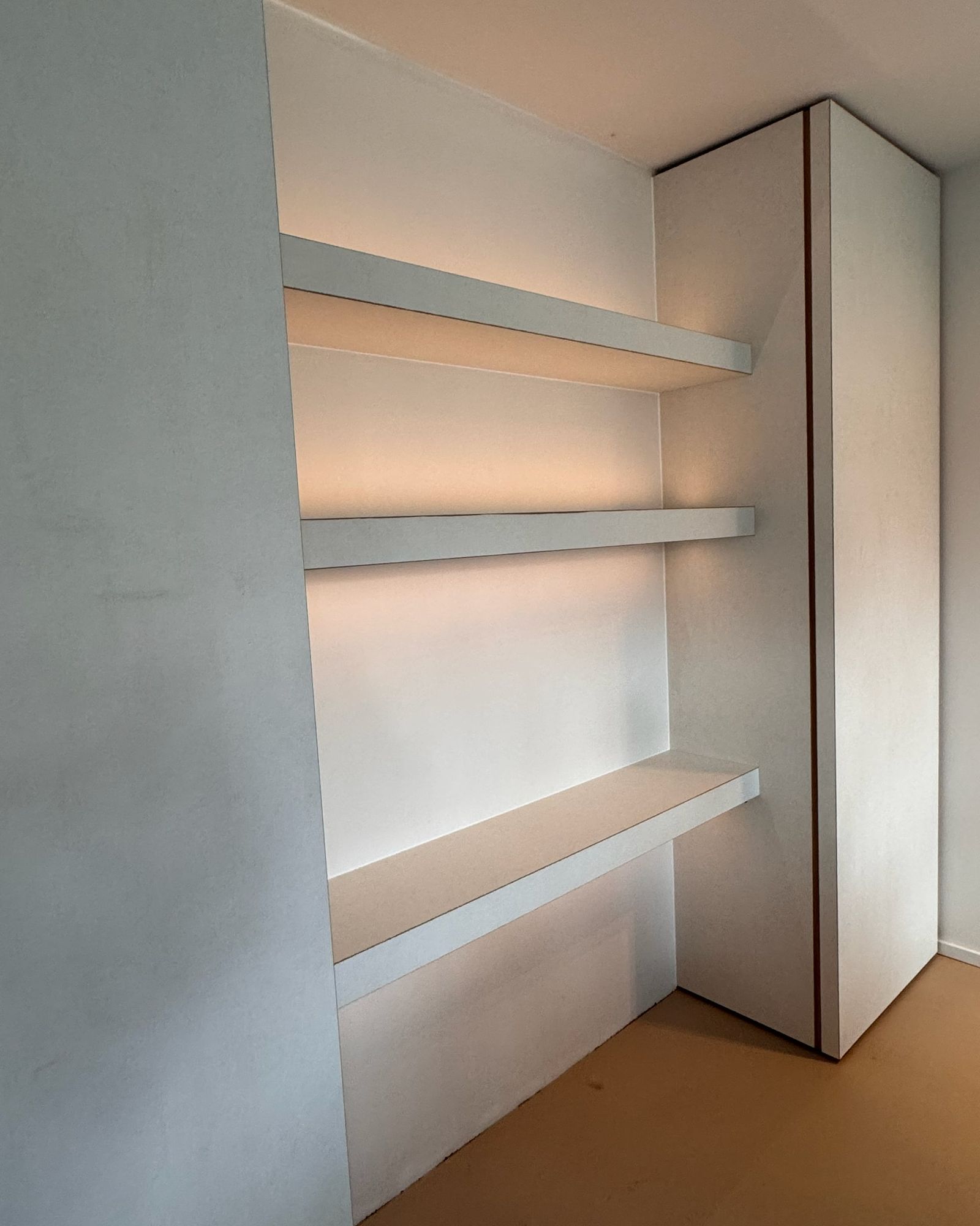 Drie dikke witte zwevende planken met warme ledverlichting eronder in een nis naast een hoge witte kolomkast