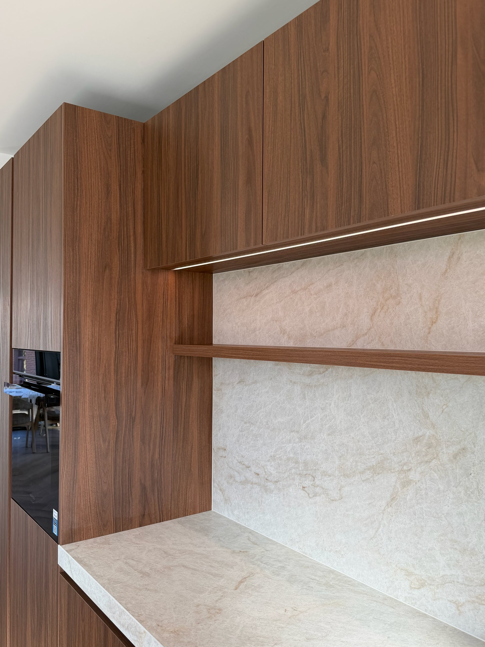 Nis in de keukenwand met stenen achterwand, zwevende walnoten plank en ledstrip onder de bovenkasten